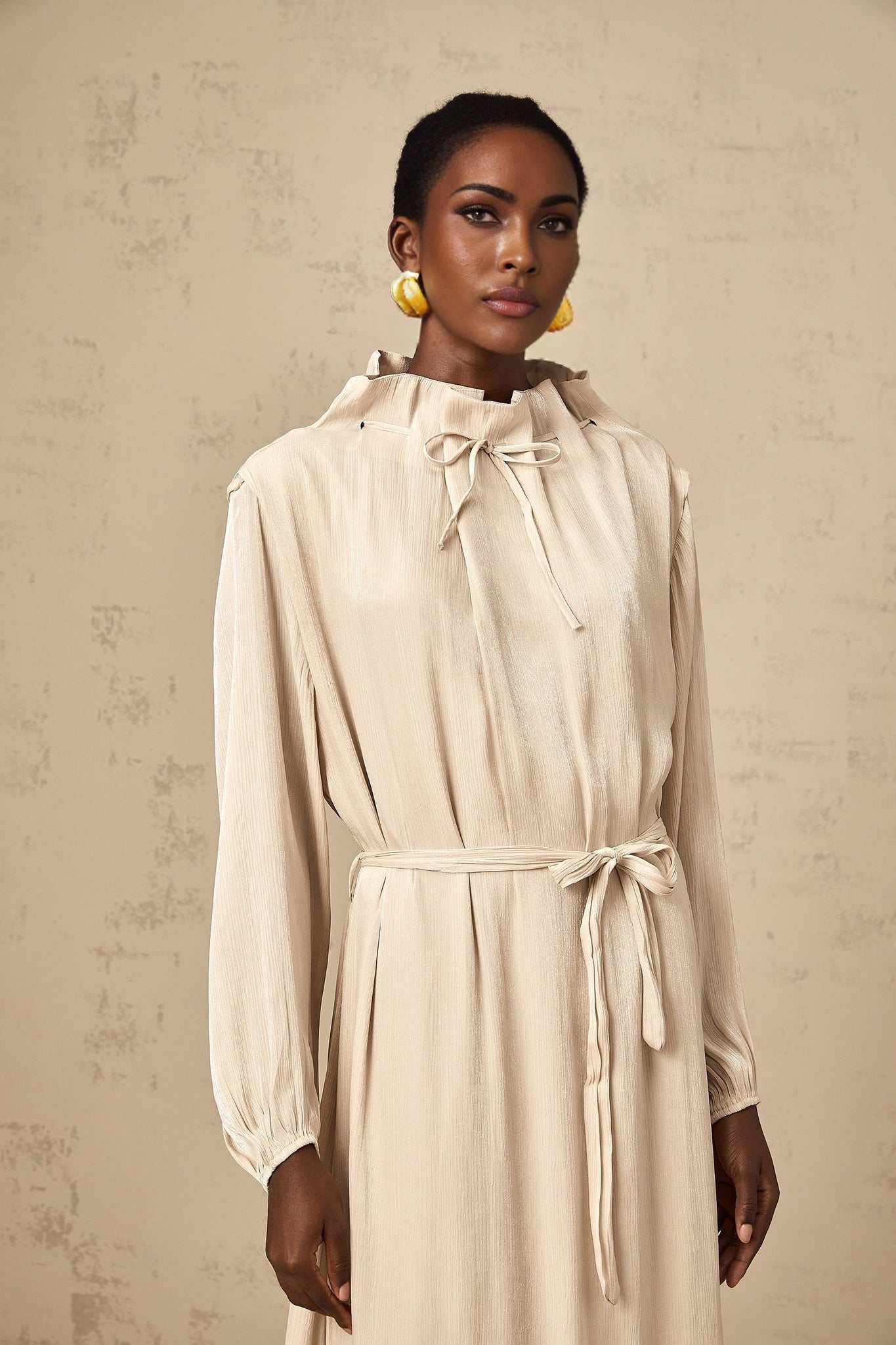 A woman wearing a lightcolored tulle midi dress with a selftie waist standing in a neutral background