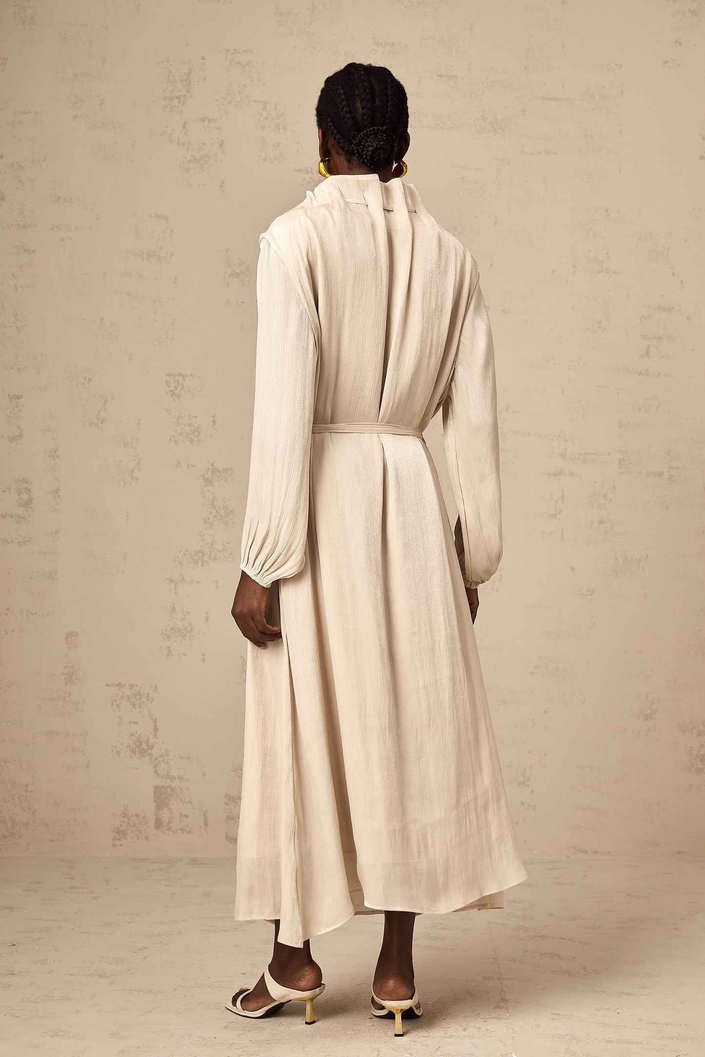 A woman wearing a lightcolored tulle midi dress with a selftie waist standing in a neutral background