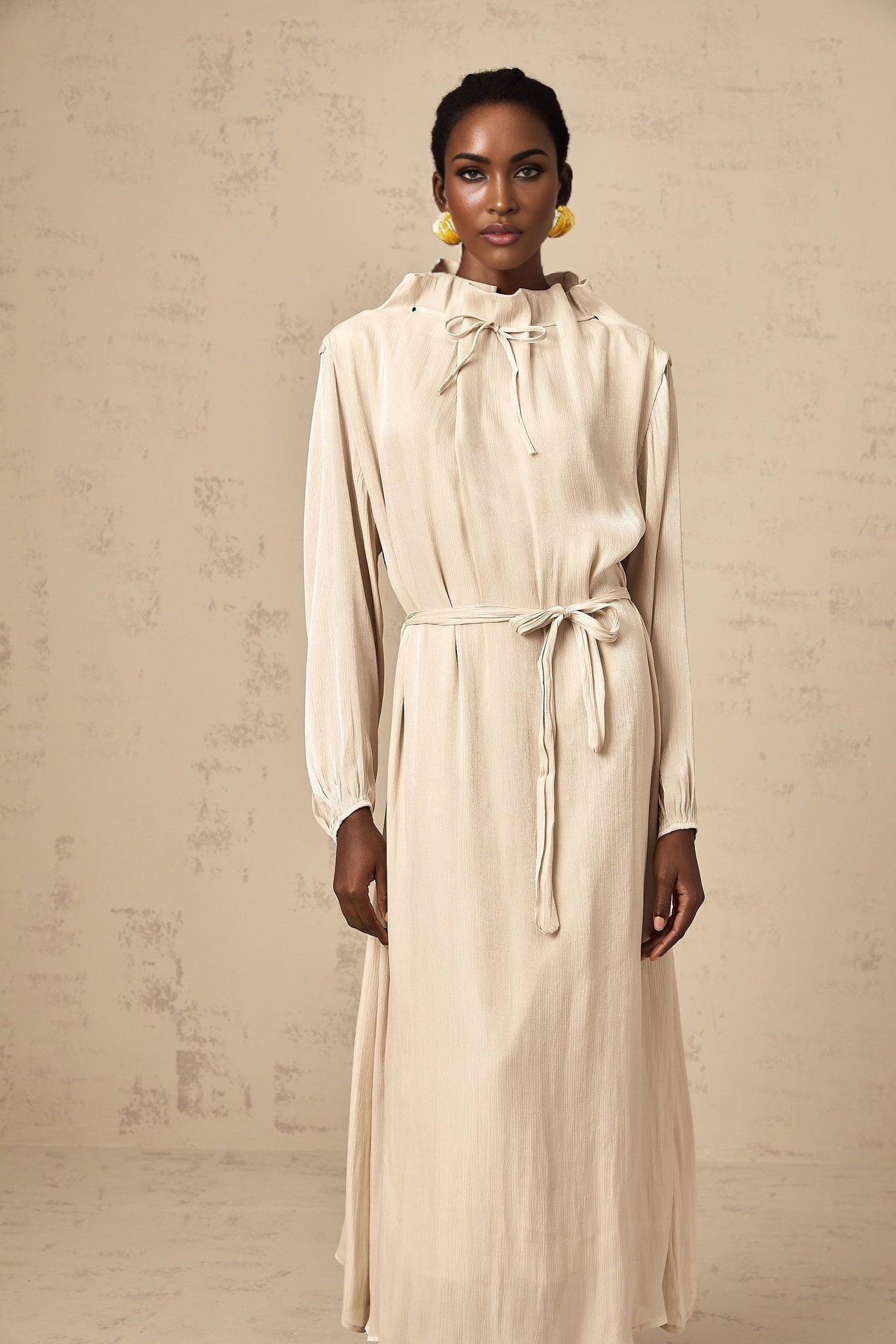 A woman wearing a lightcolored tulle midi dress with a selftie waist standing in a relaxed pose