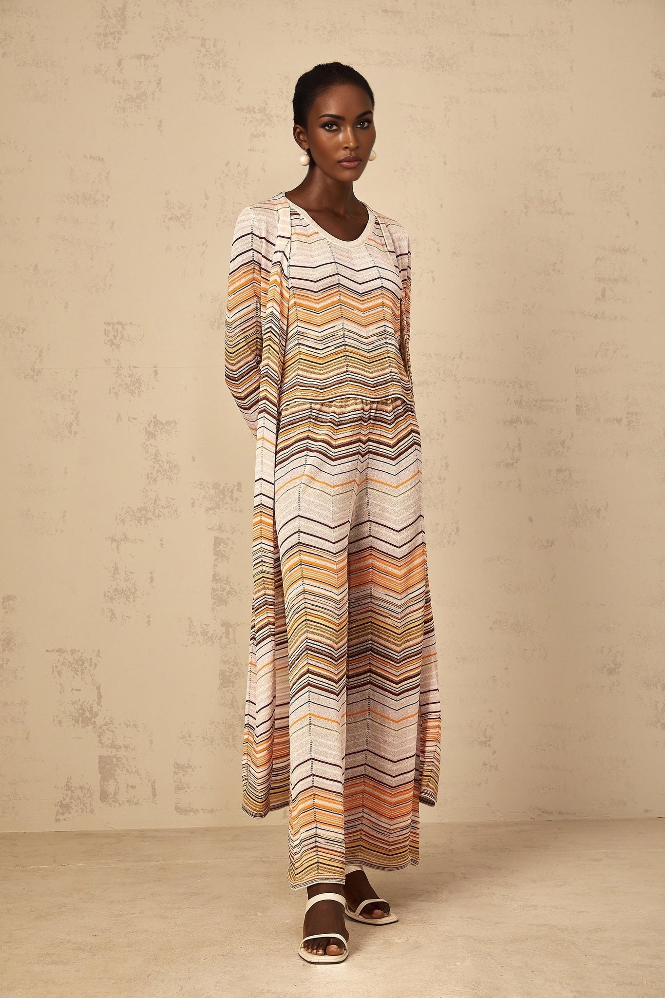 A woman wearing a long beige and white striped knit cardigan from Chloe standing against a plain background