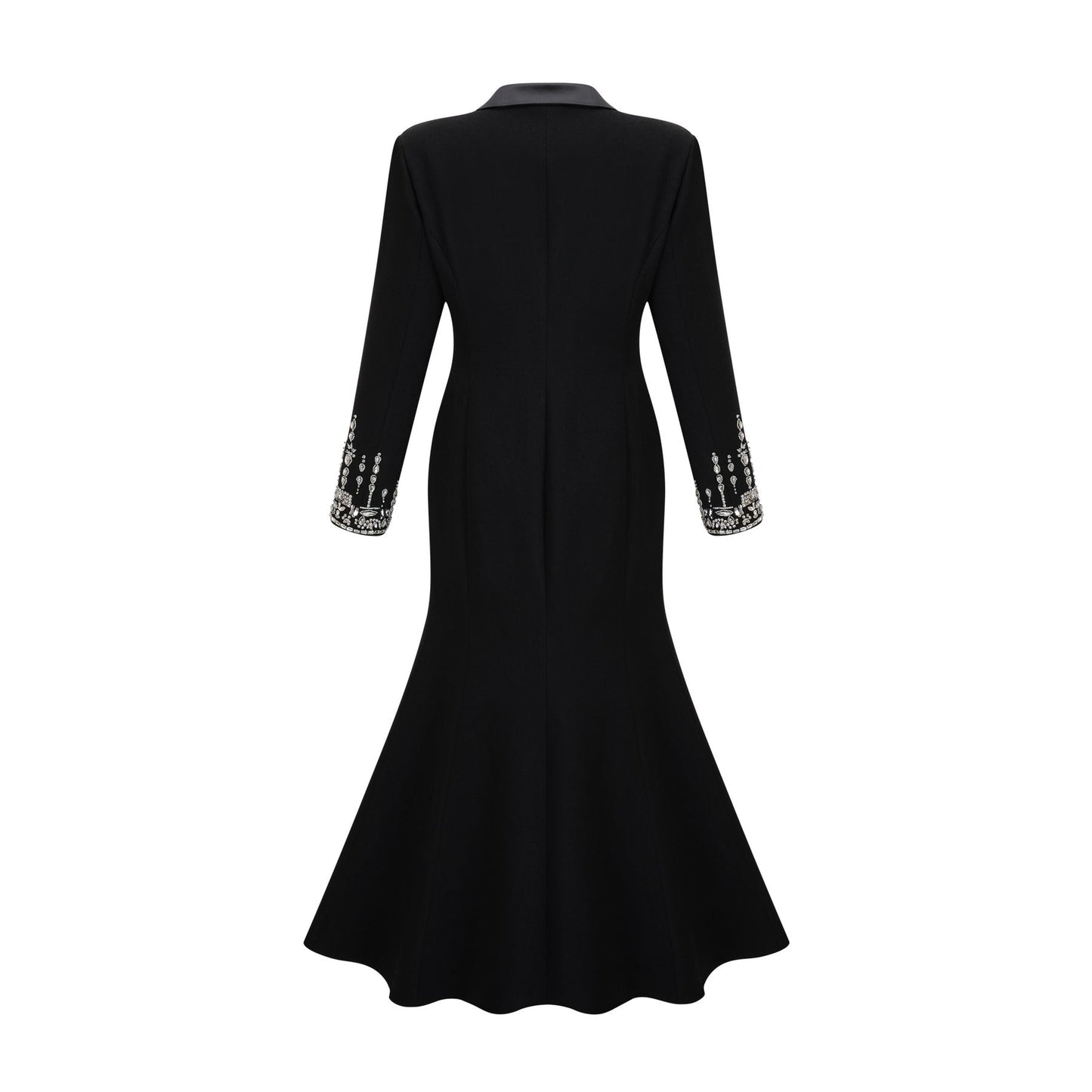 A woman wearing a long black blazer dress with embellishments standing in a relaxed pose against a plain background