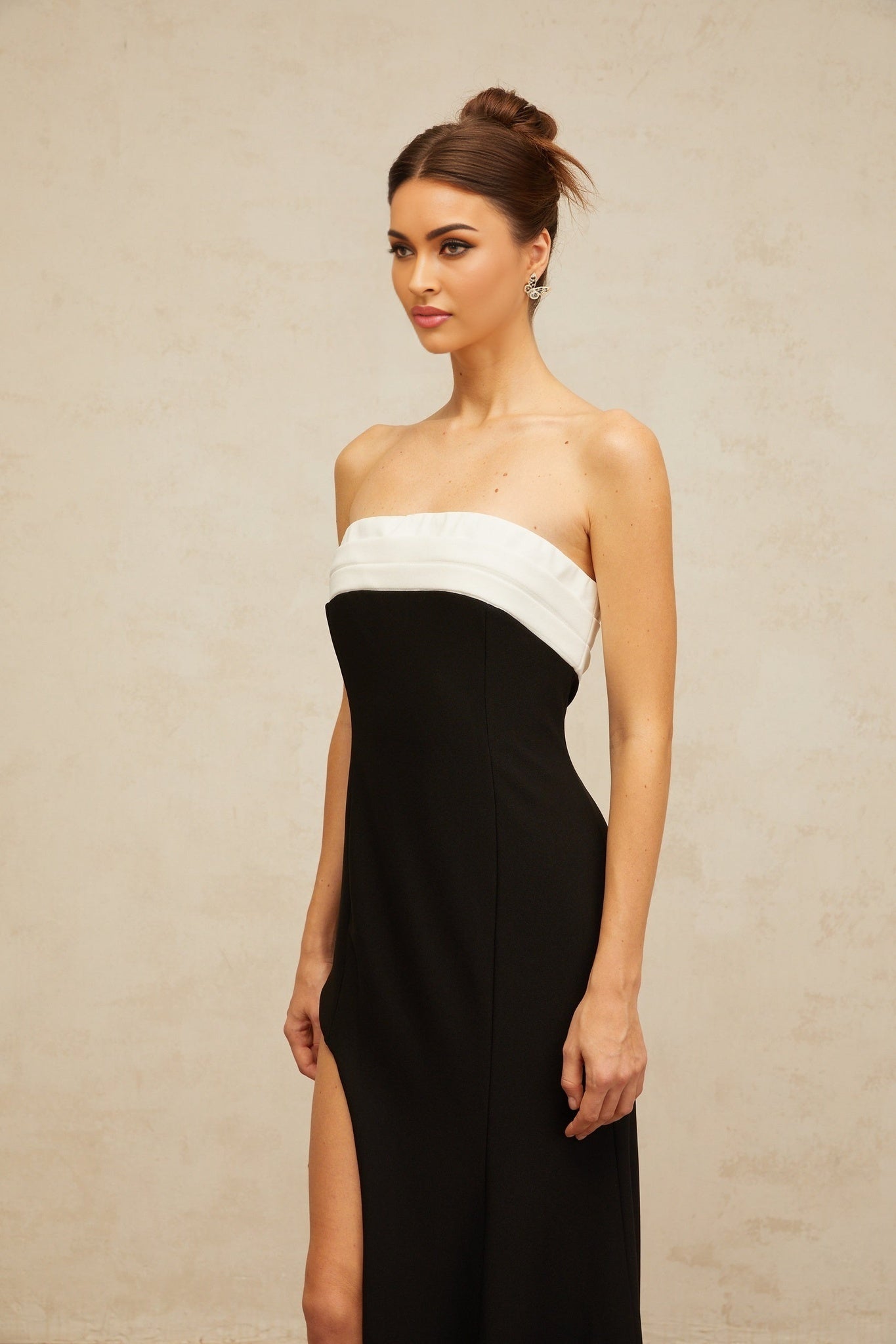 A woman wearing a long black maxi dress with a contrasting color block design and an offshoulder neckline