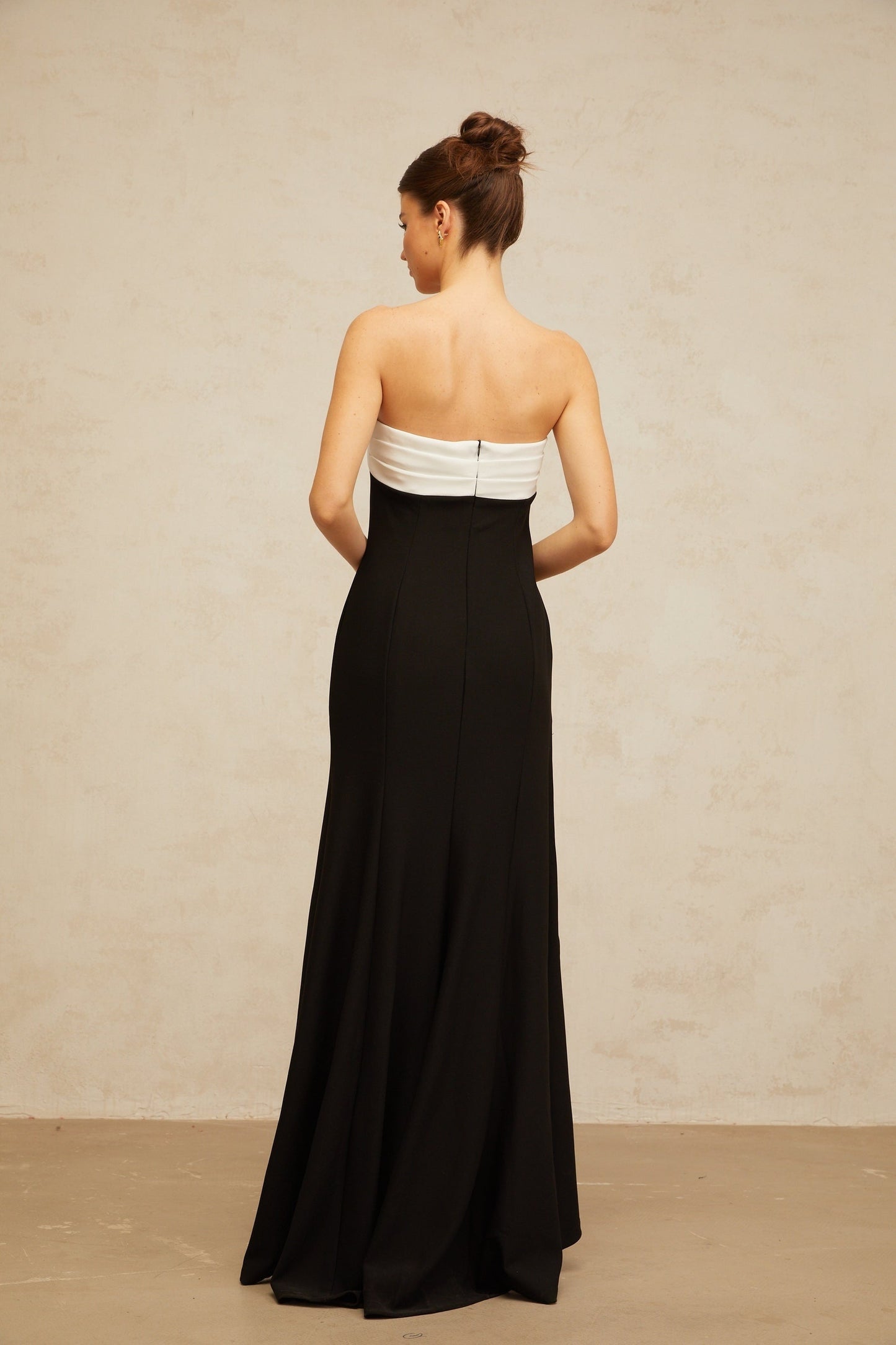 A woman wearing a long black maxi dress with contrasting color blocks and an offshoulder neckline