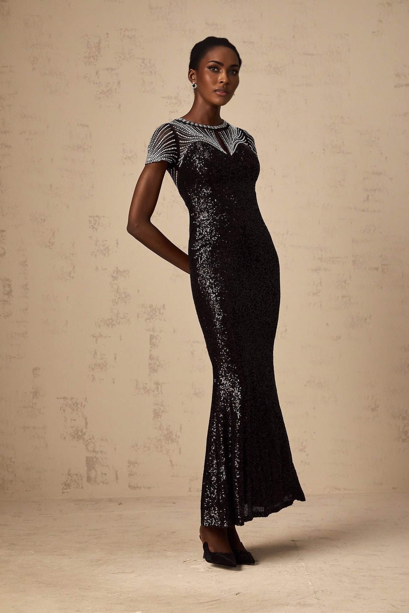 A woman wearing a long black maxi dress with sequin details and cut out sections