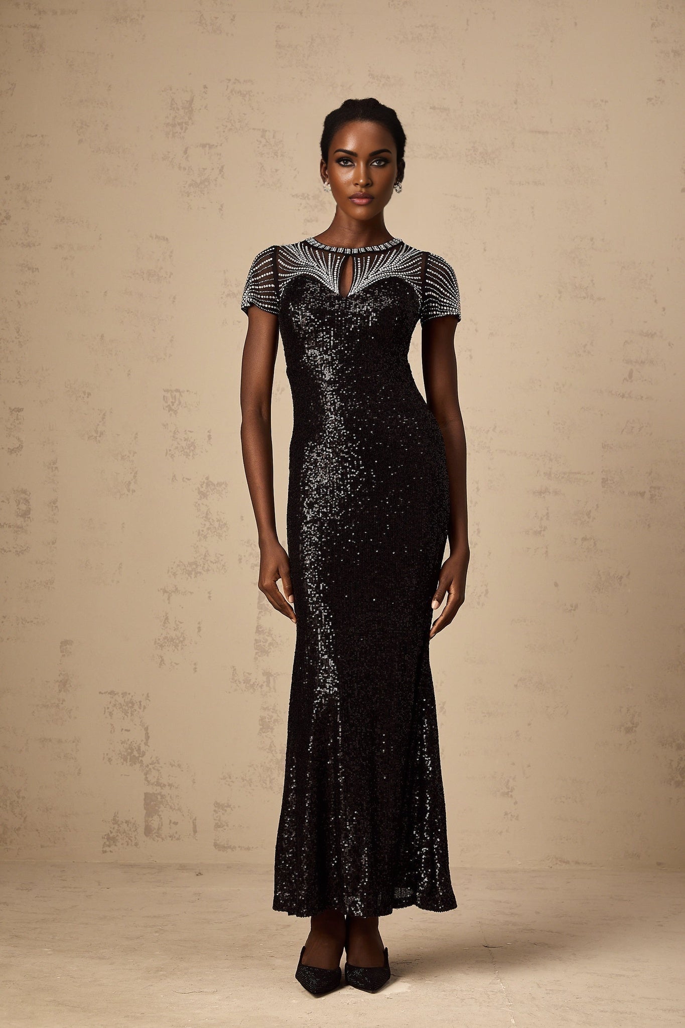 A woman wearing a long black maxi dress with sequin details and cutout sections