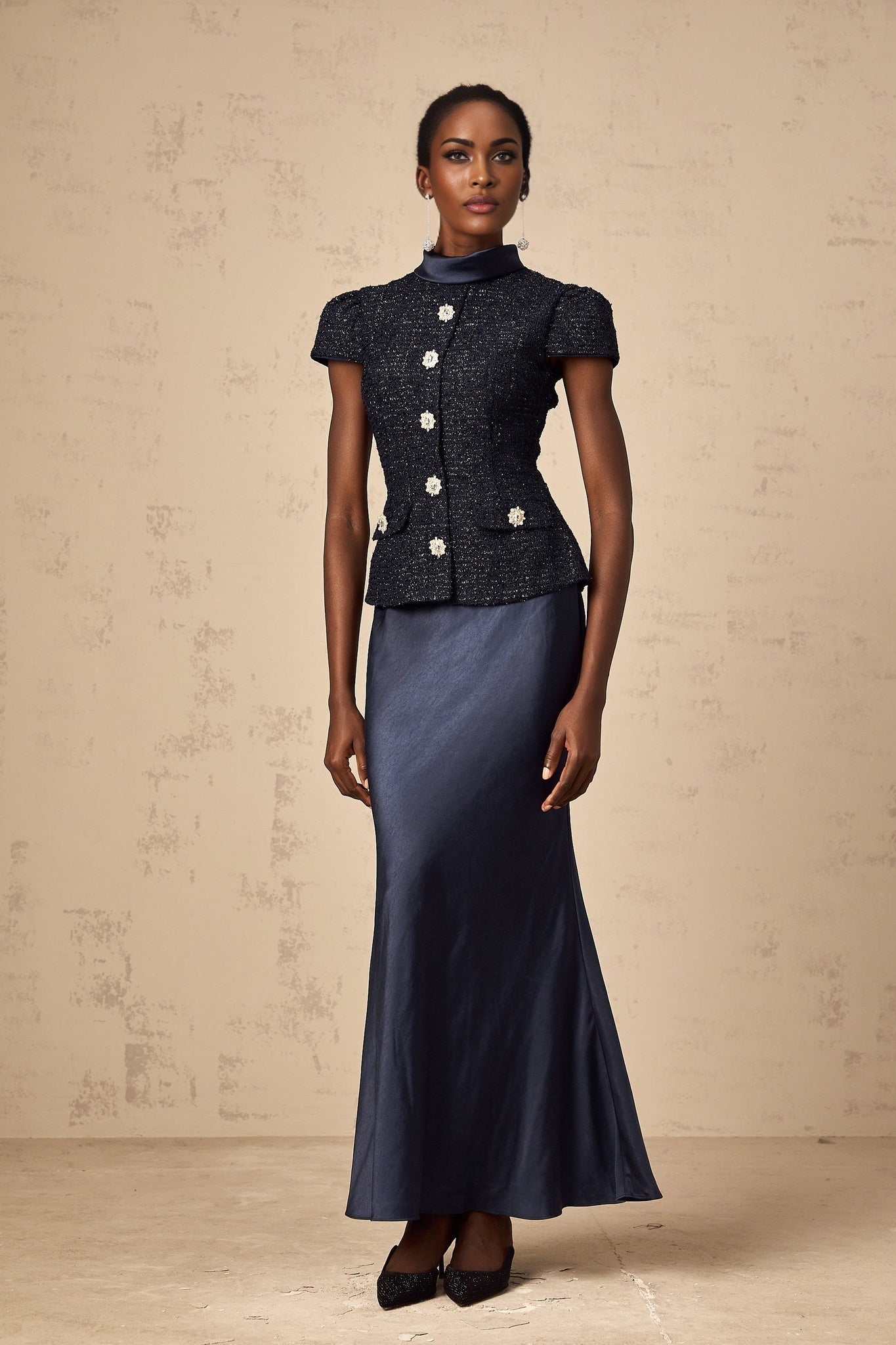A woman wearing a long blue maxi dress with a fitted peplum waist and panelled design featuring a flowy skirt and sleeveless bodice