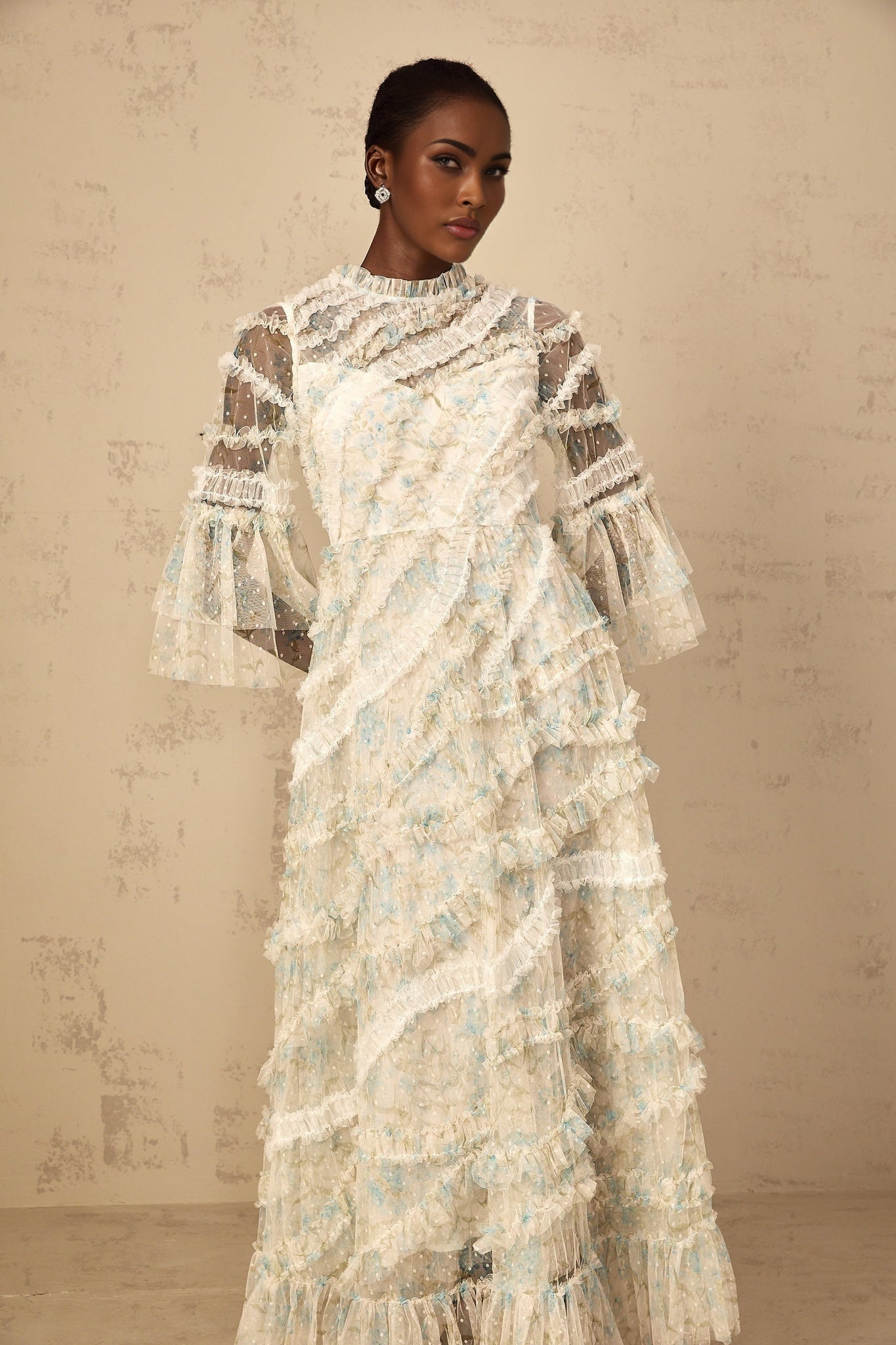 A woman wearing a long blue maxi dress with a floral print pattern and ruffled tulle details