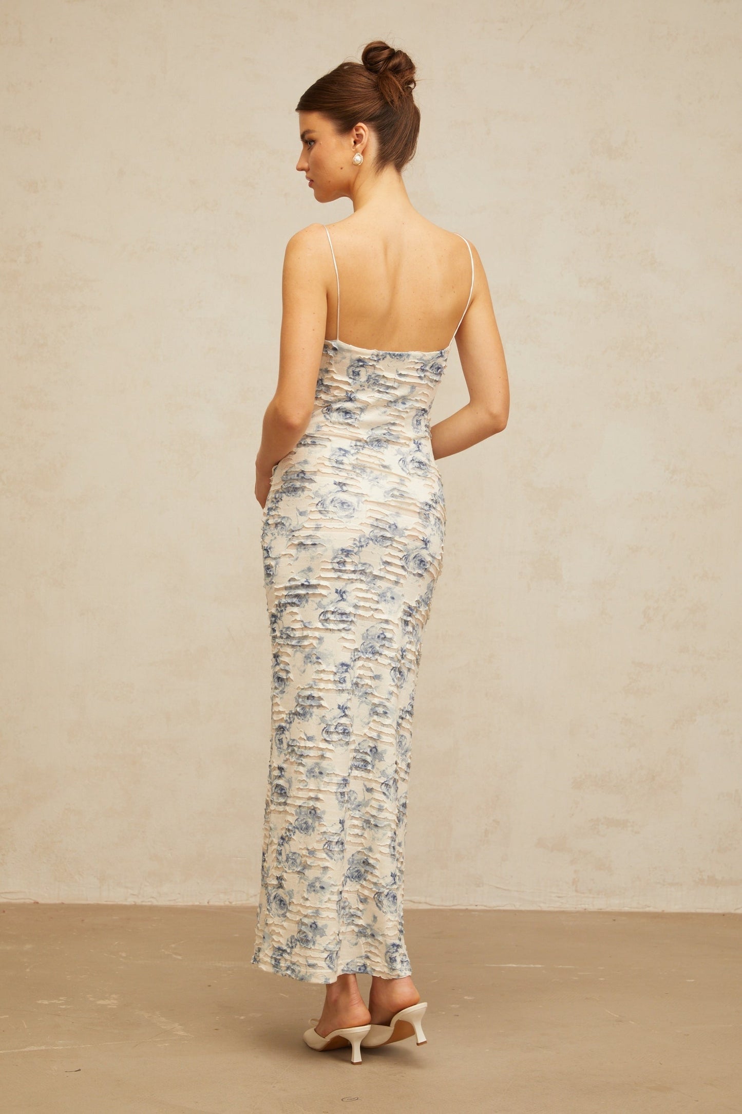 A woman wearing a long blue maxi dress with a textured floral print pattern The dress features a flowing silhouette and extends to the floor