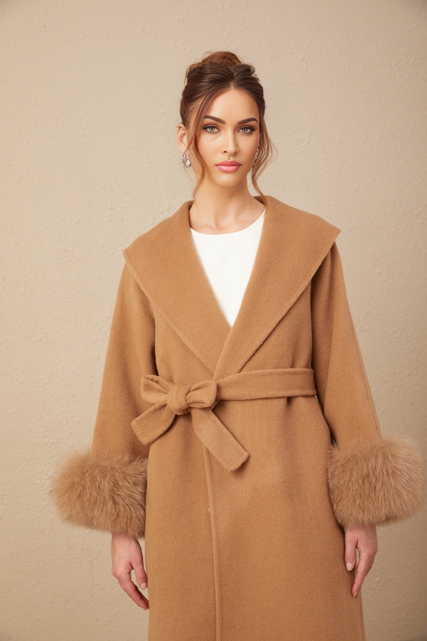 A woman wearing a long brown woolen wrap overcoat with a felted texture standing against a plain background