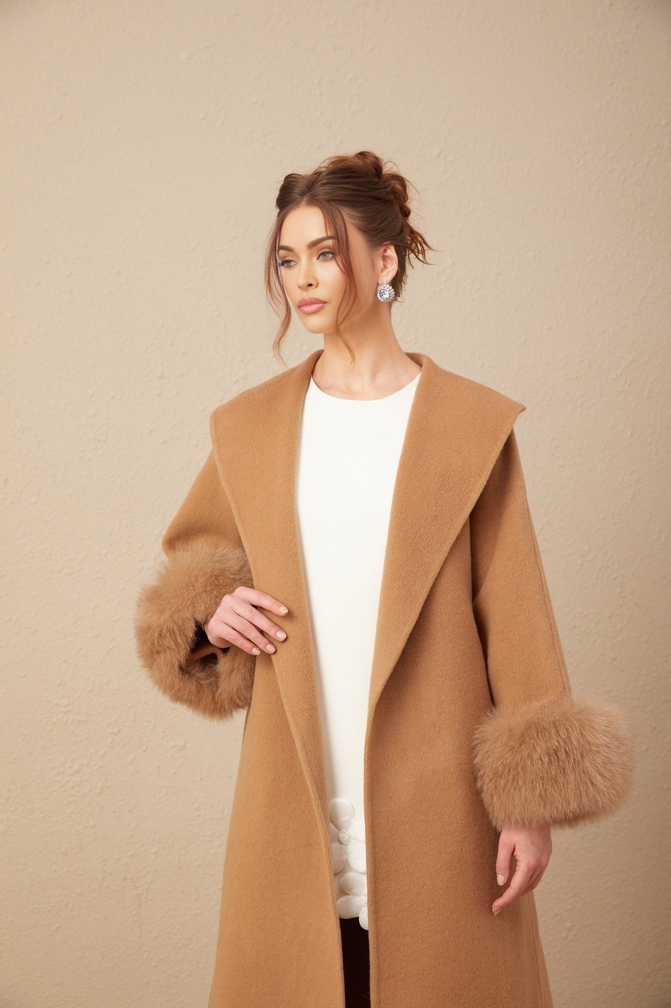 A woman wearing a long brown woolen wrap overcoat with a felted texture standing against a plain background