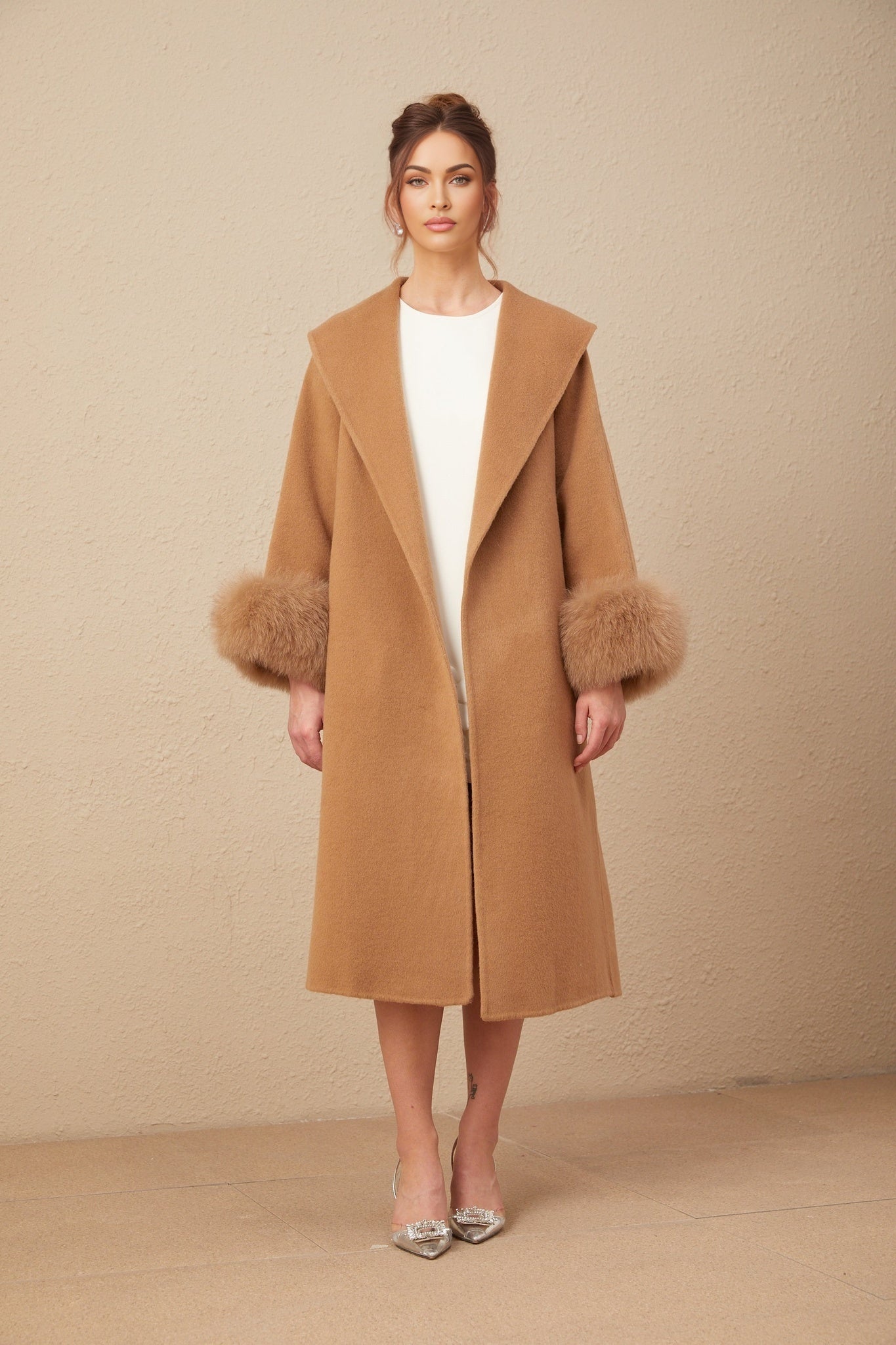 A woman wearing a long brown woolen wrap overcoat with a felted texture standing against a plain background
