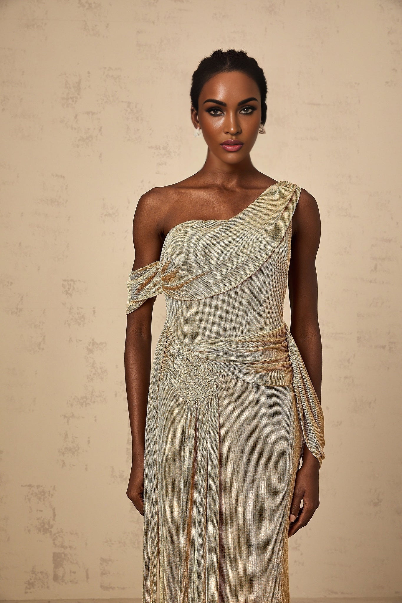 A woman wearing a long flowing gold maxi dress with a gathered waist and ribbon design details