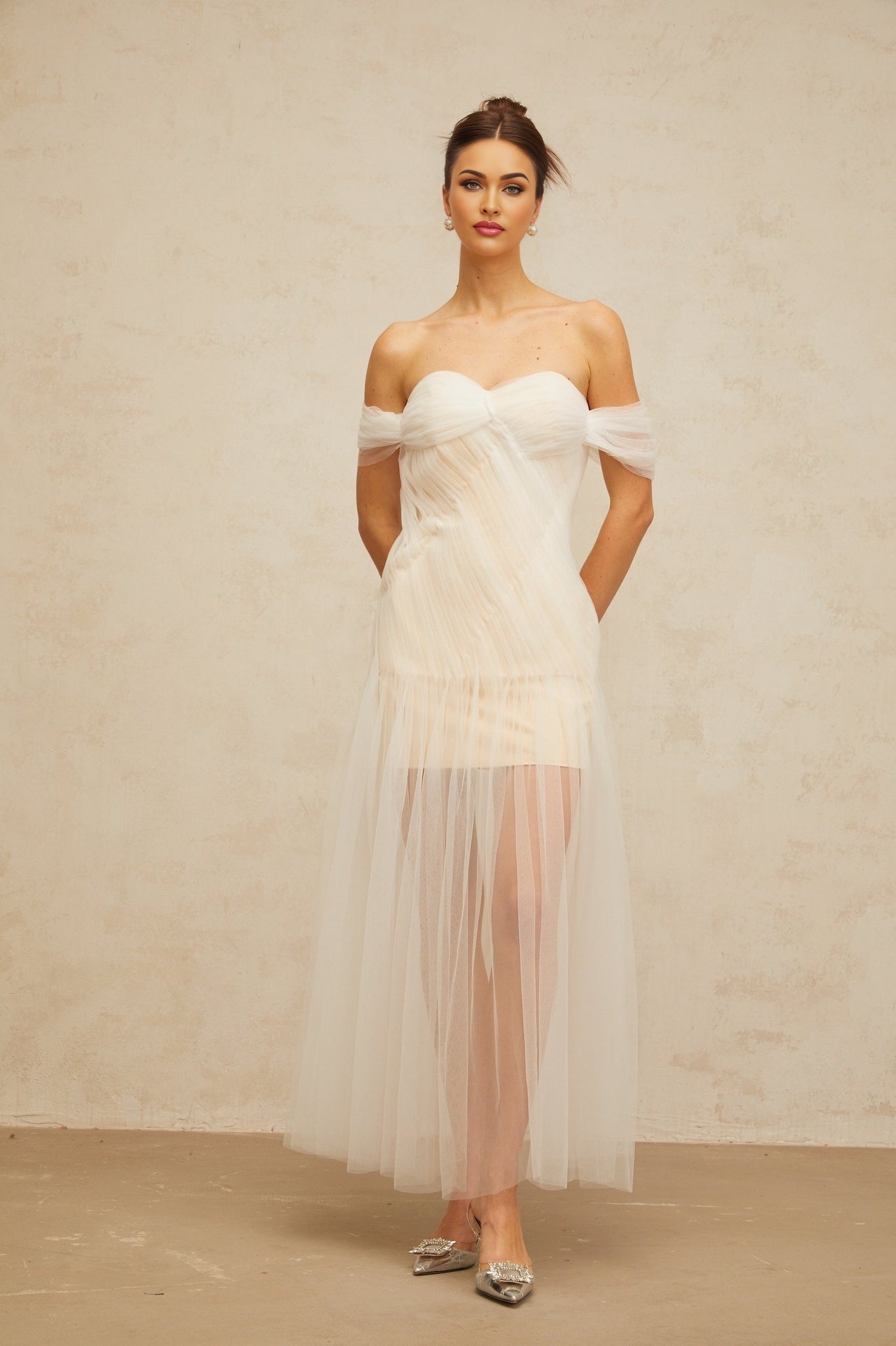 A woman wearing a long flowing off white maxi dress with pleated tulle fabric the dress has a fitted bodice and flared skirt creating an elegant silhouette