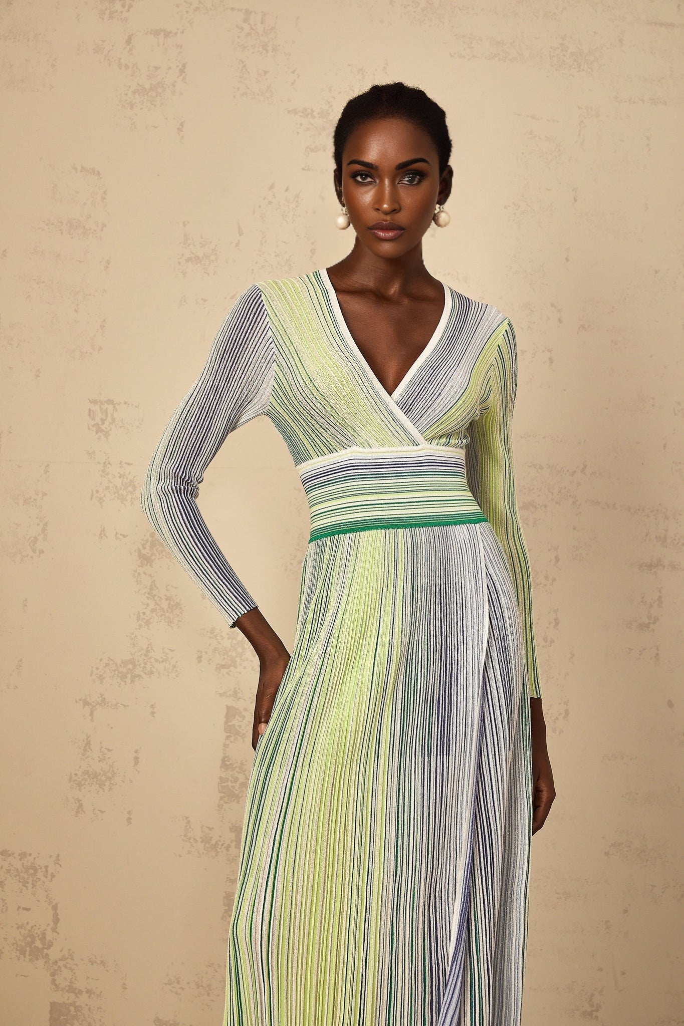 A woman wearing a long green knit maxi dress with long sleeves and horizontal sequin stripes sparkling throughout the dress