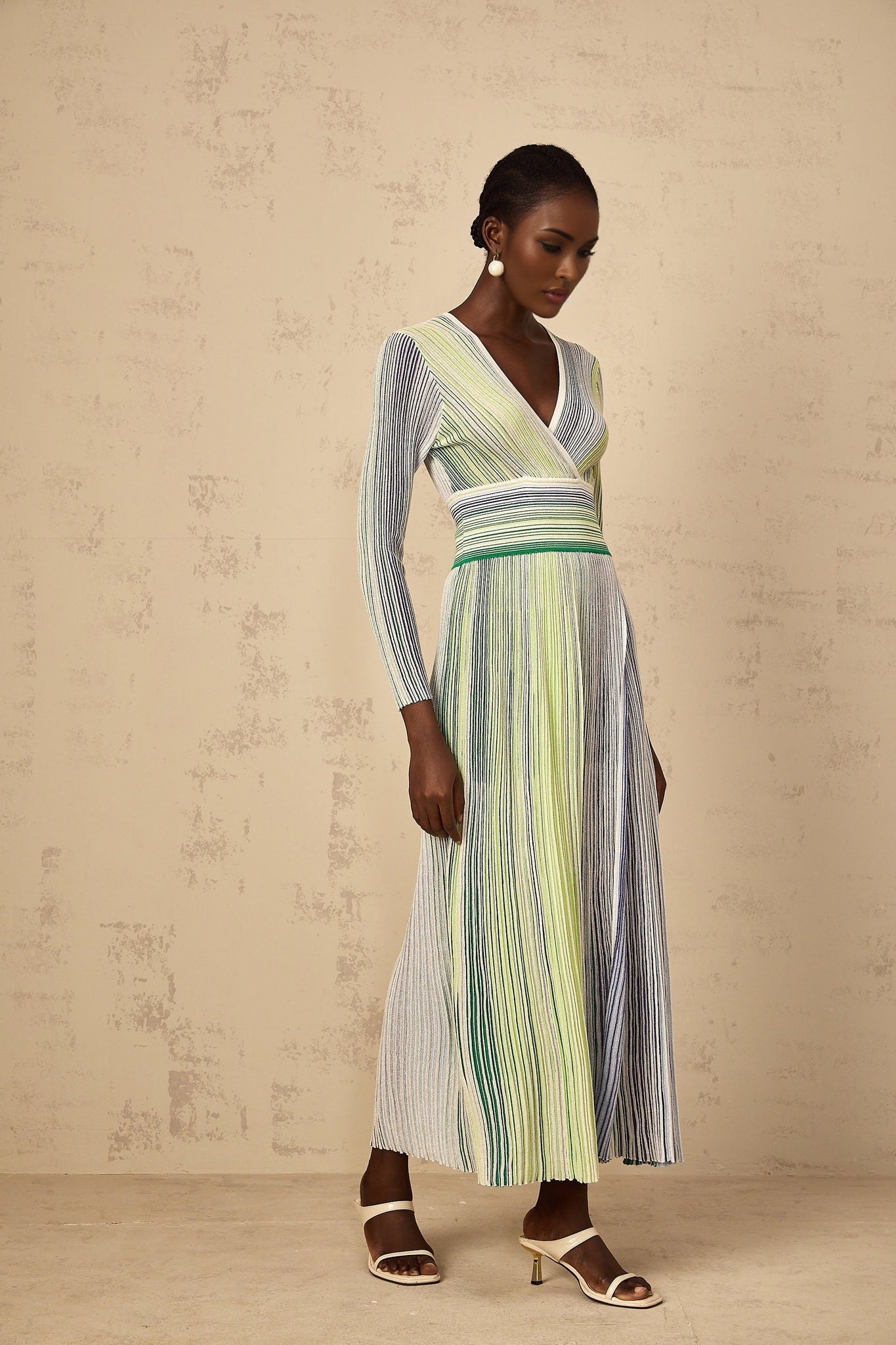 A woman wearing a long green maxi dress with long sleeves and vertical sequin stripes running down the length of the dress