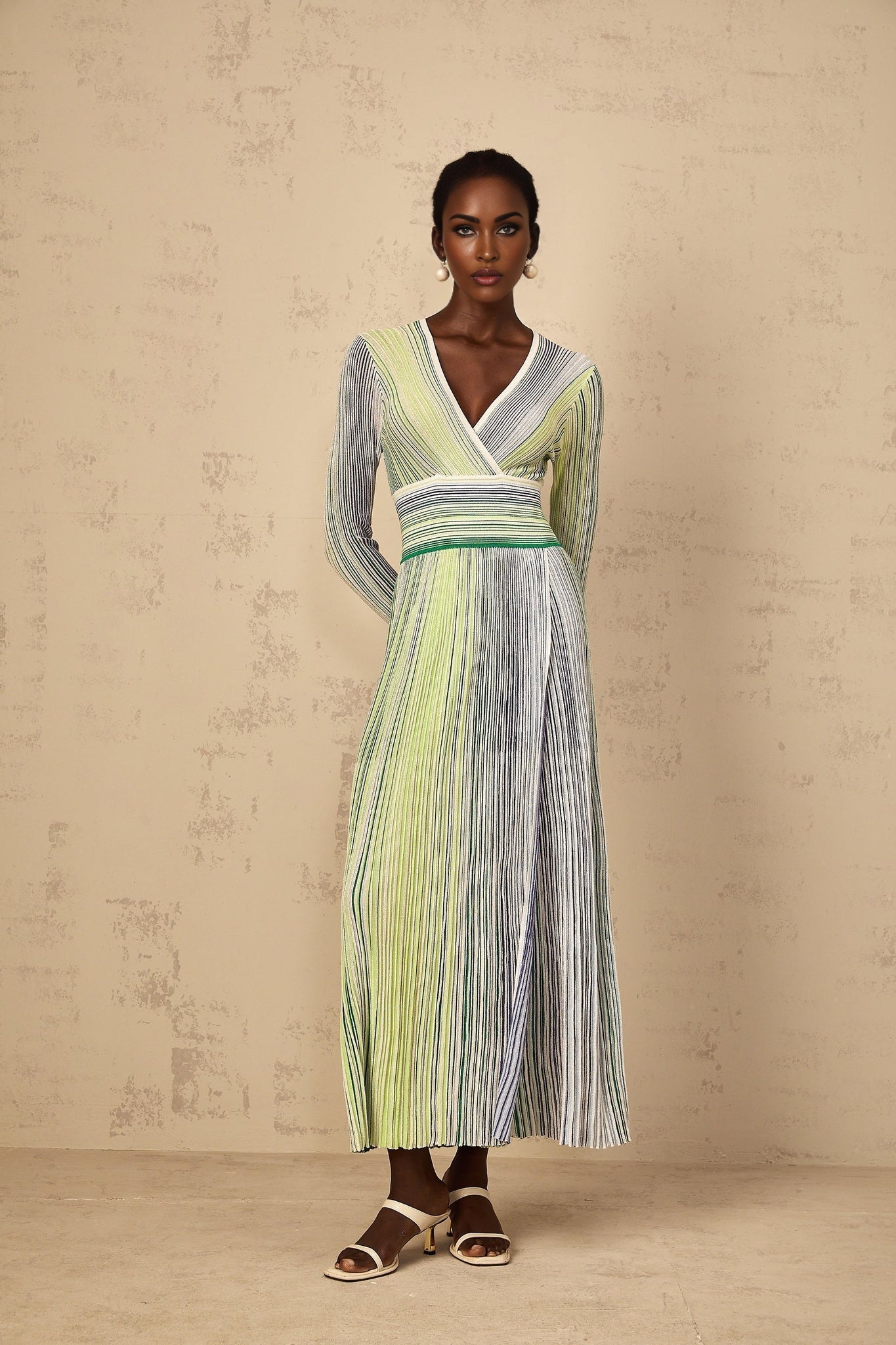 A woman wearing a long green maxi dress with long sleeves and vertical sequin stripes standing in a relaxed pose