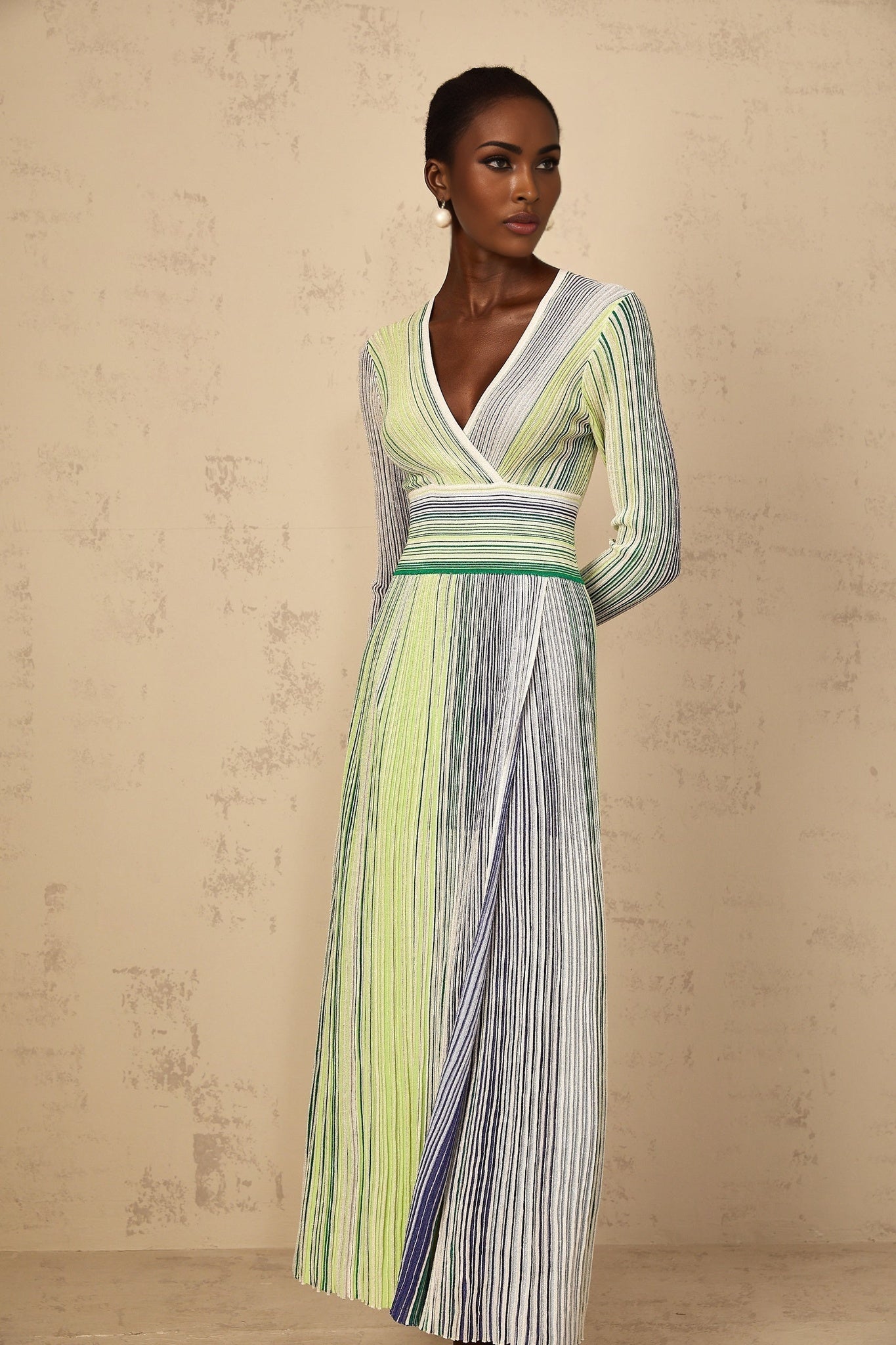 A woman wearing a long green maxi dress with long sleeves featuring sequin striped detailing and a knit fabric
