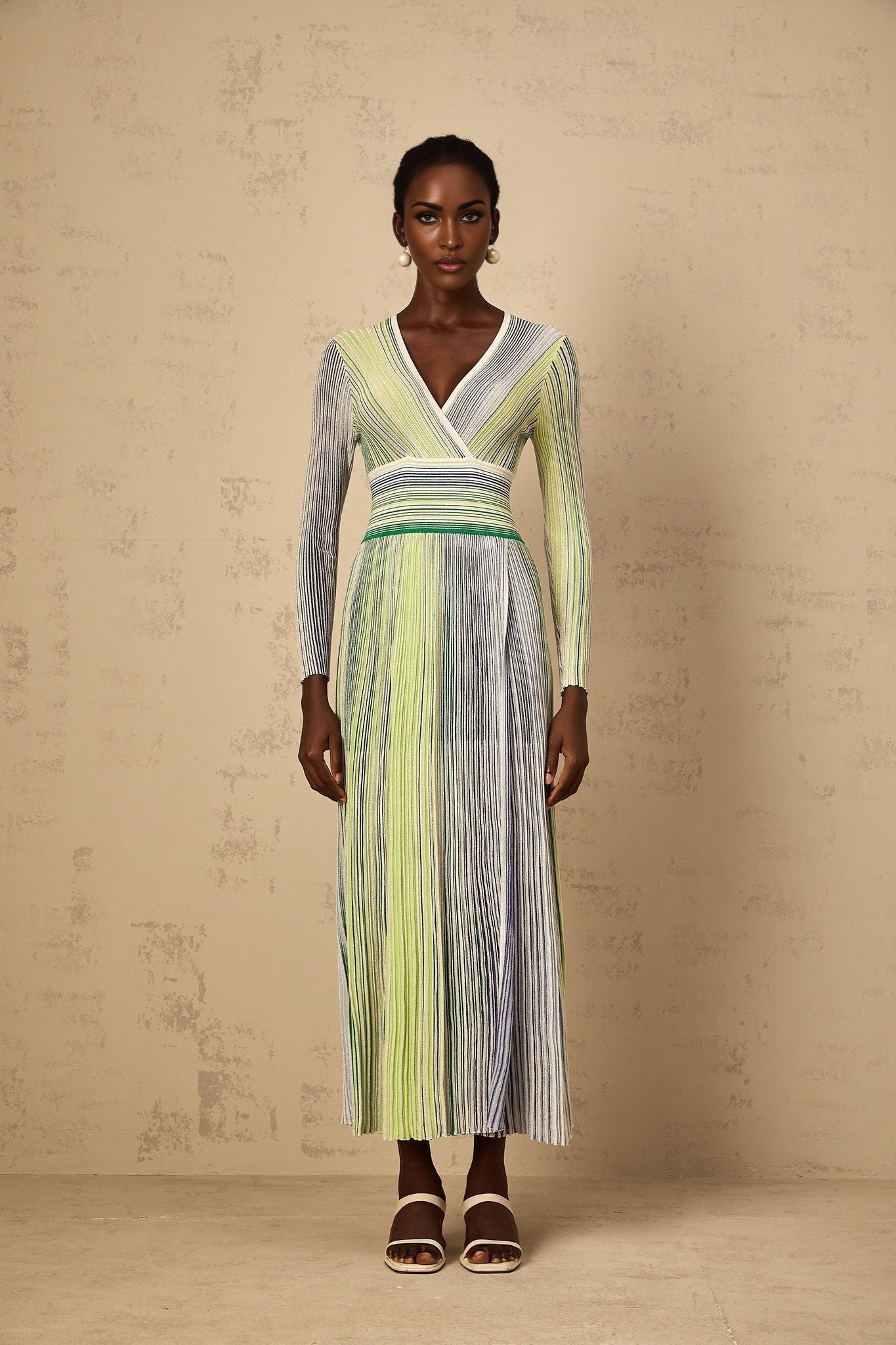 A woman wearing a long green maxi dress with long sleeves featuring sequin stripes along the length of the dress