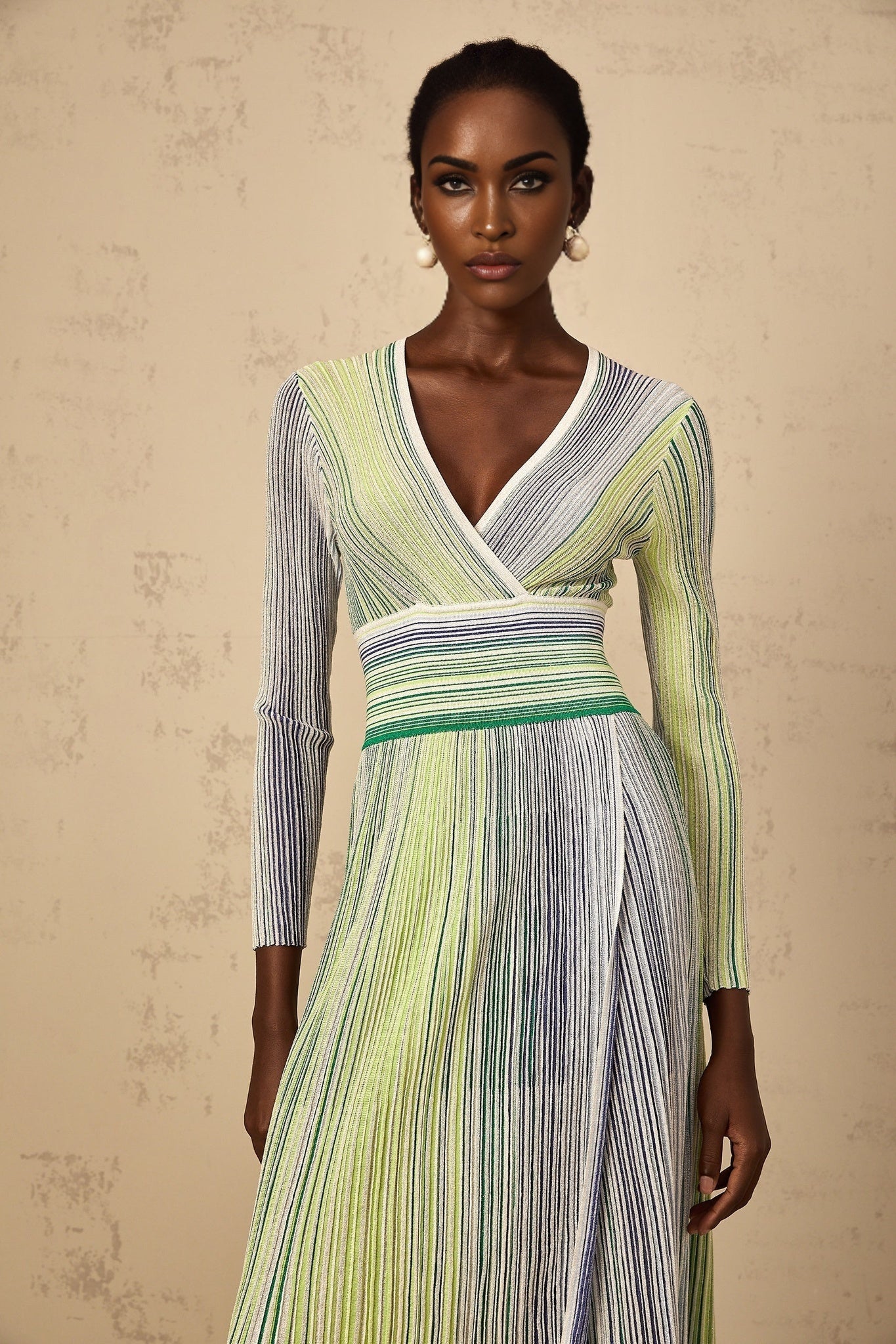 A woman wearing a long green maxi dress with long sleeves featuring sequin stripes and a knit texture