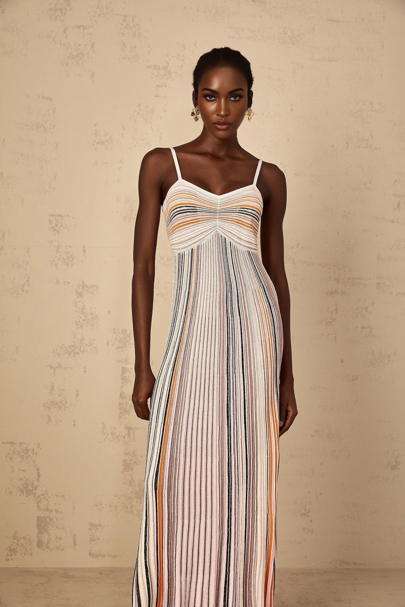 A woman wearing a long knit maxi dress with alternating neutral and sequin striped pattern