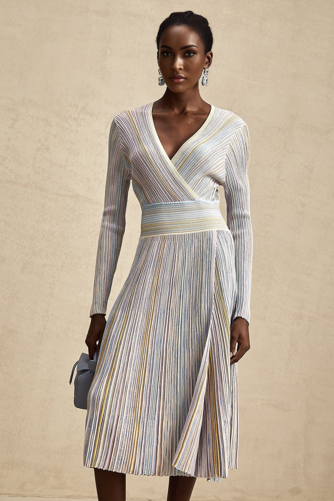 A woman wearing a long knitted midi dress with vertical stripes standing in a casual pose