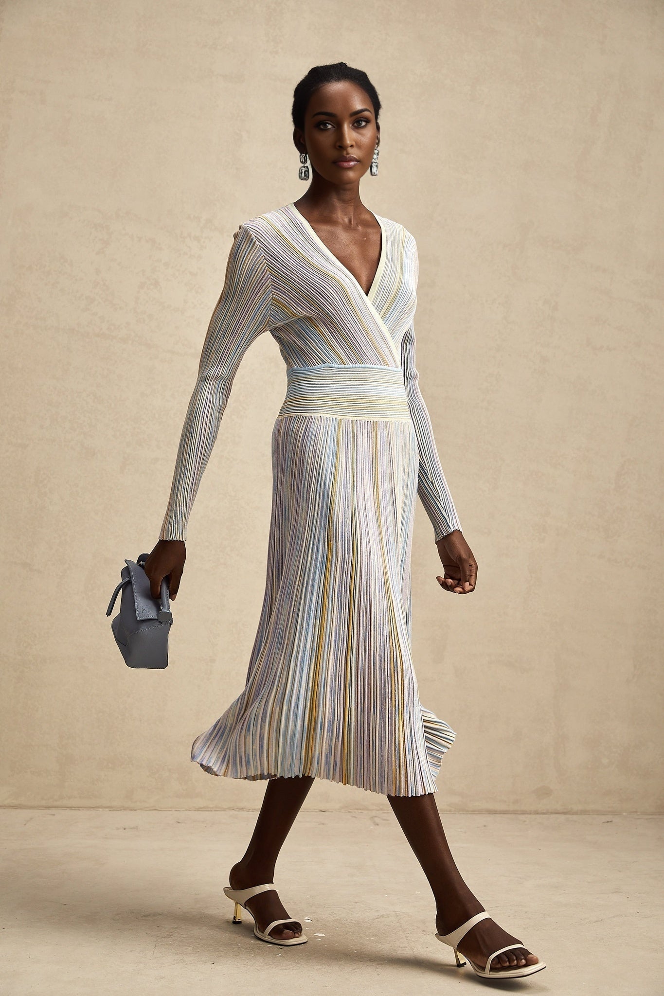 A woman wearing a long knitted midi dress with vertical stripes standing in a neutral background The dress features alternating light and dark stripes and has a fitted silhouette
