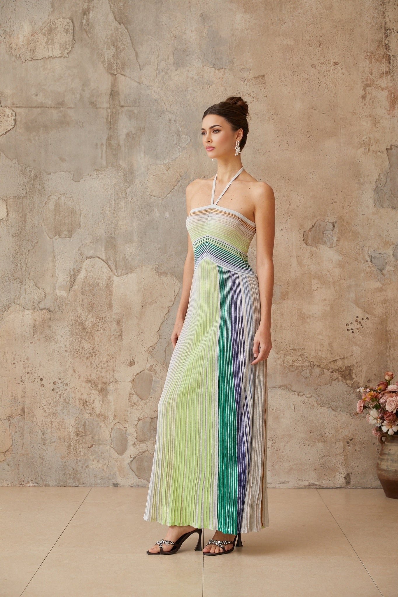 A woman wearing a long metallic knit backless maxi dress with a shimmering finish standing in a relaxed pose