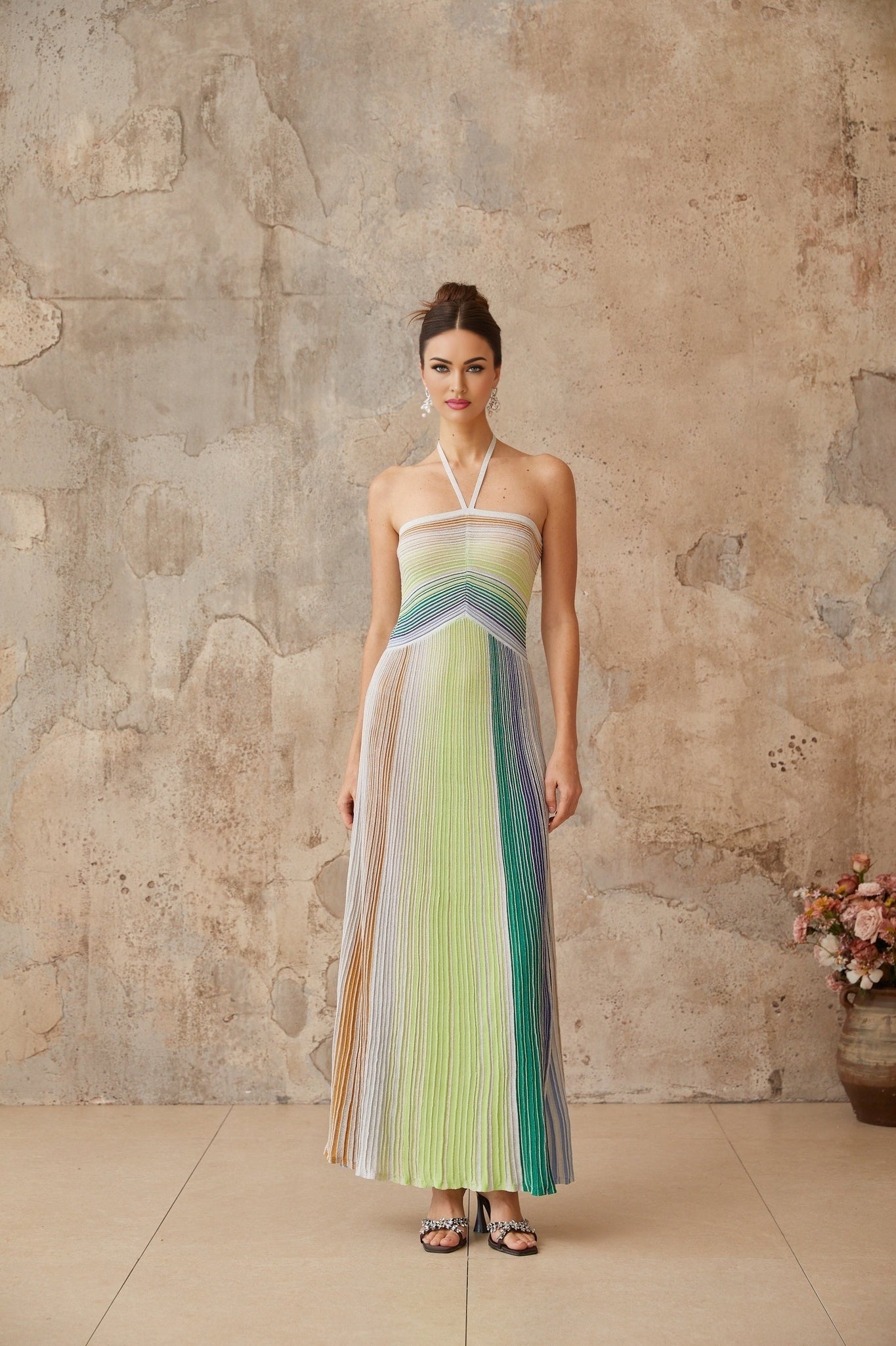 A woman wearing a long metallic knit maxi dress with a backless design standing in a relaxed pose showing off the shimmering fabric and elegant silhouette