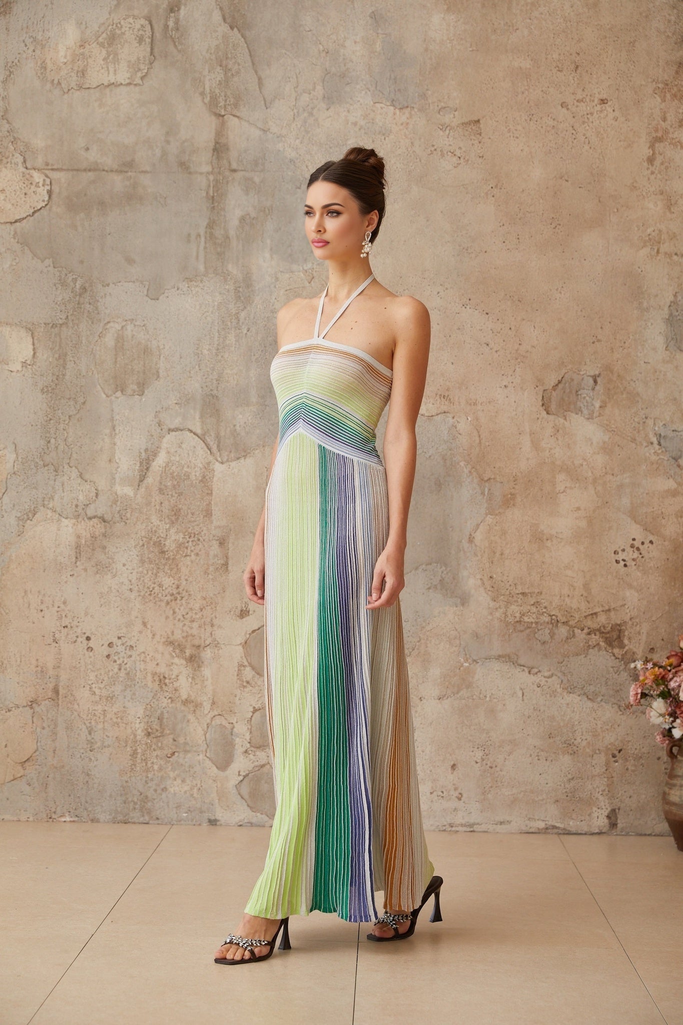 A woman wearing a long metallic knit maxi dress with a backless design standing in a relaxed pose