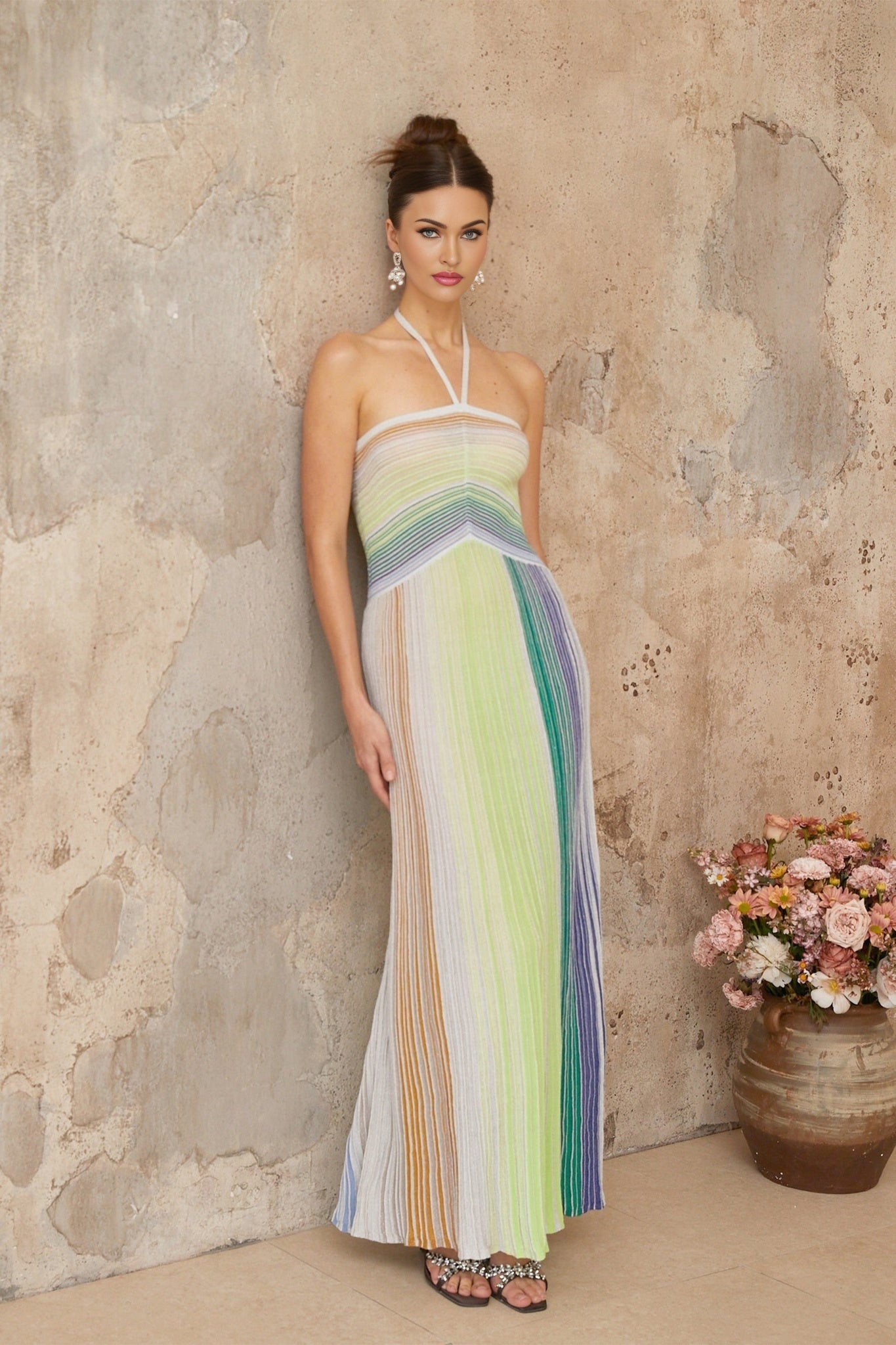 A woman wearing a long metallic knit maxi dress with a backless design standing in a relaxed pose