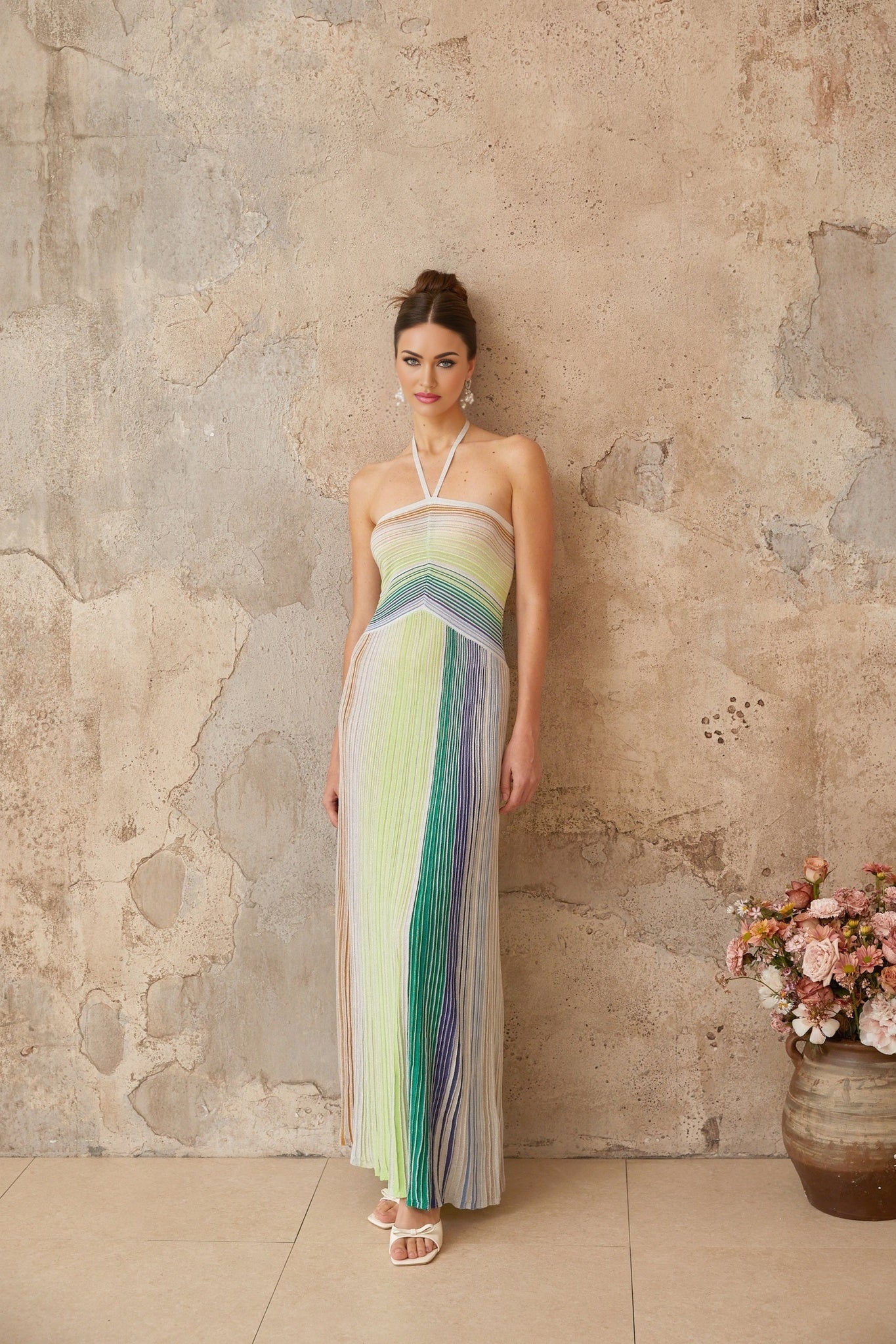 A woman wearing a long metallic knit maxi dress with a backless design standing in a stylish pose