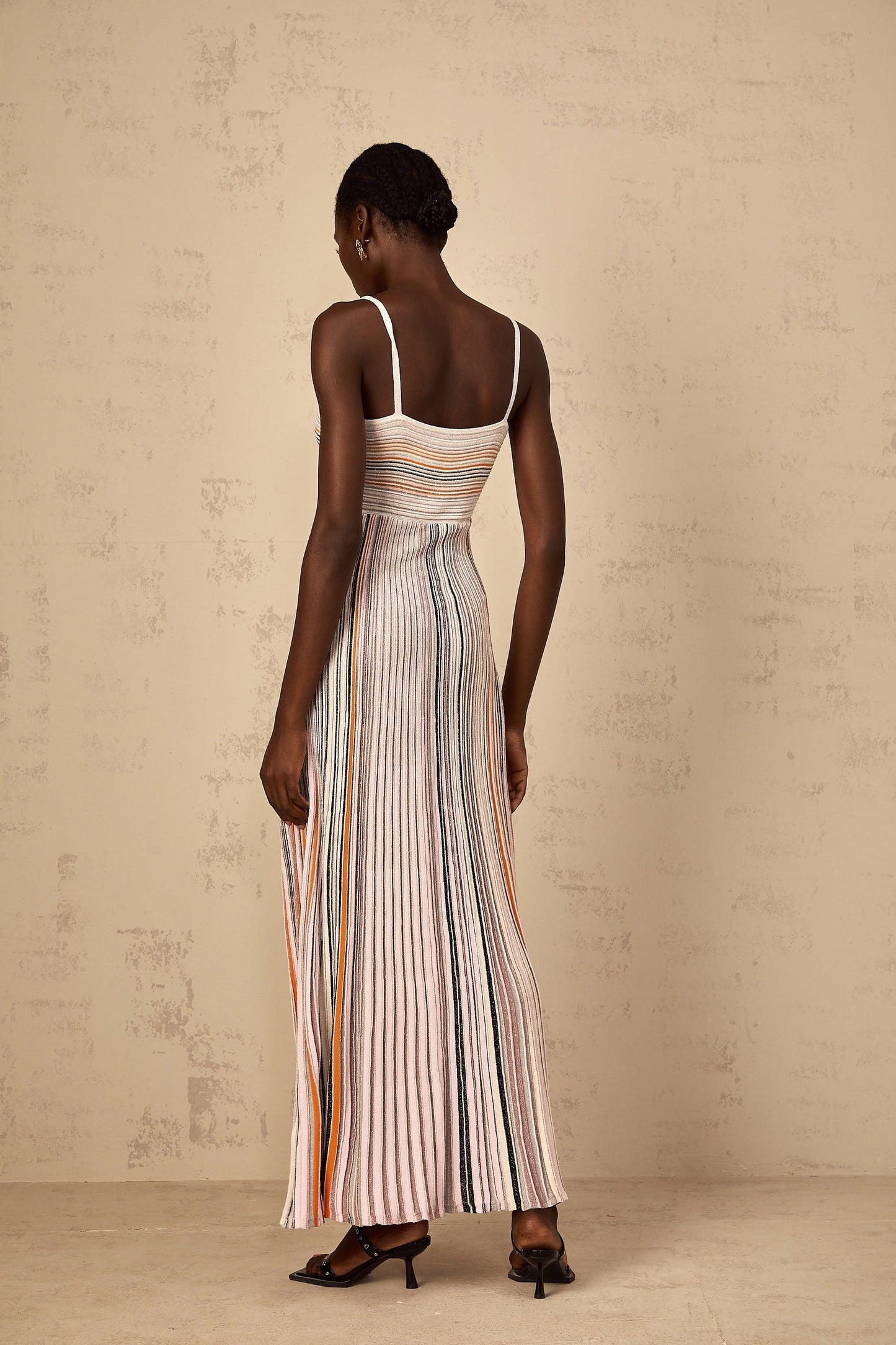 A woman wearing a long neutral colored maxi dress with horizontal sequin stripes knitted into the fabric