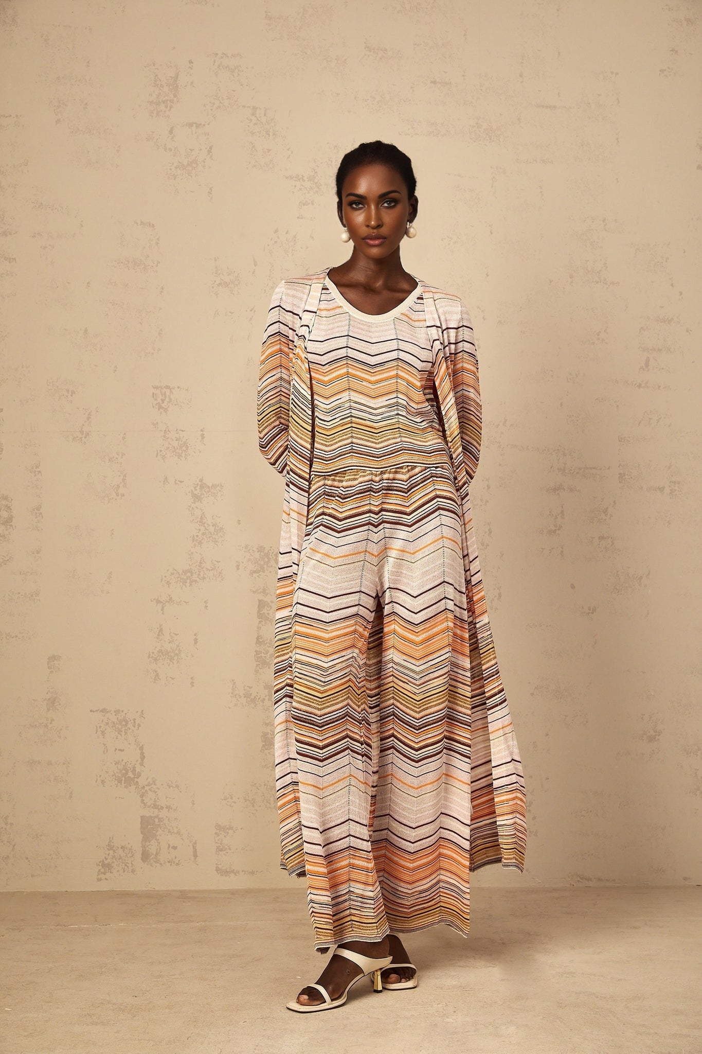 A woman wearing a long neutral striped knit cardigan from Chloe standing in a relaxed pose
