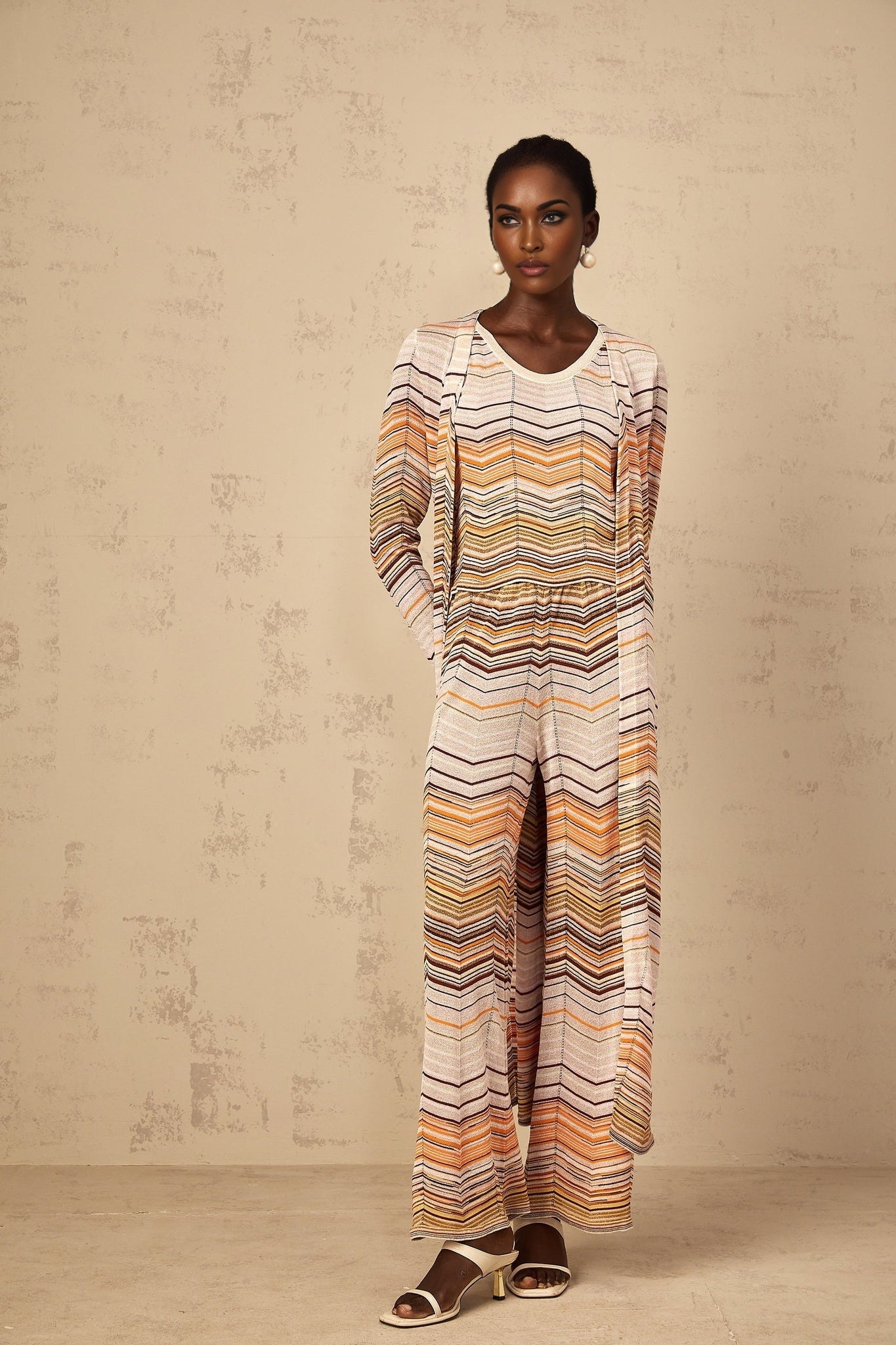 A woman wearing a long neutraltoned striped knit cardigan from Chloe standing in a relaxed pose