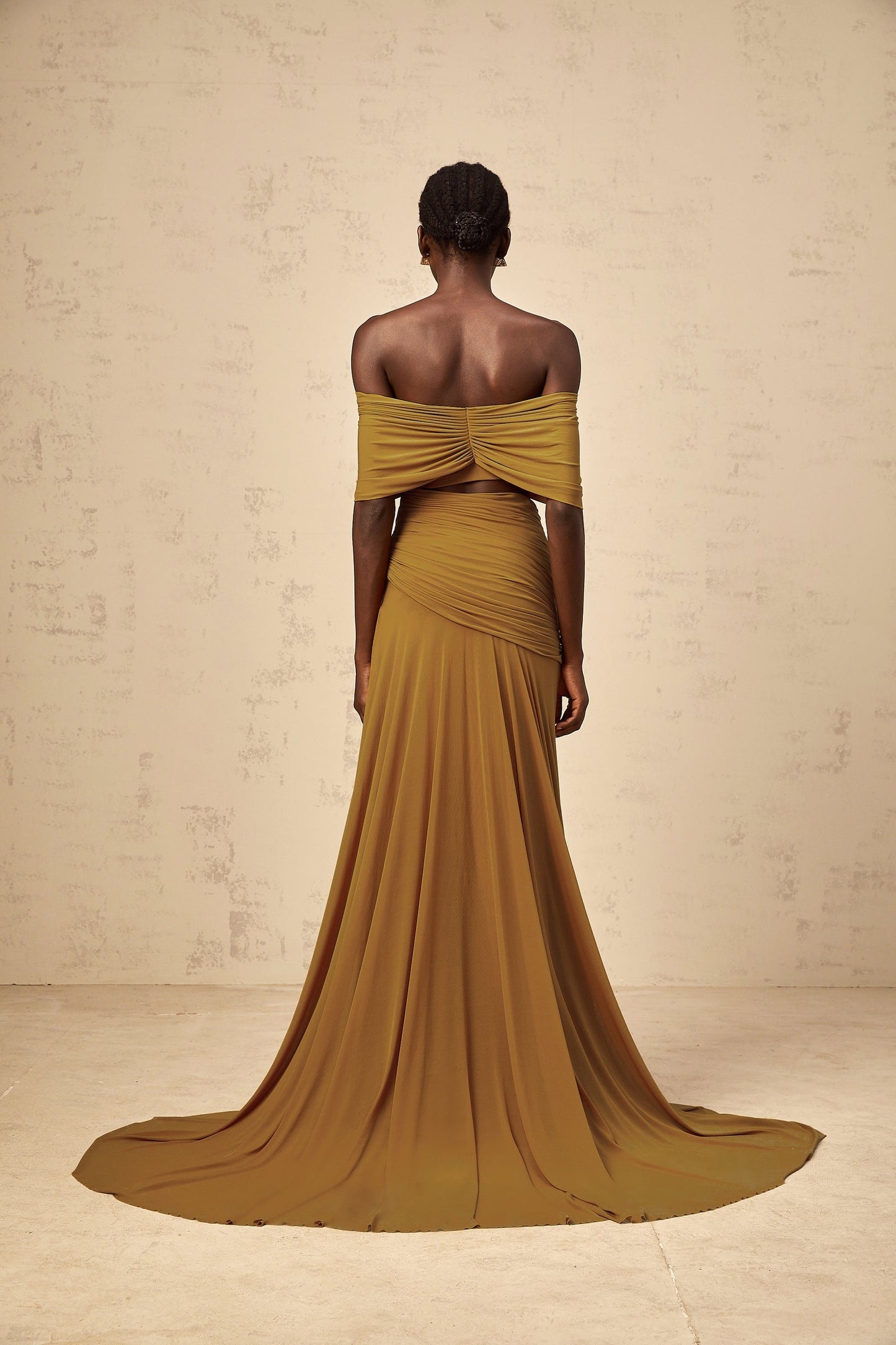 A woman wearing a long ocher maxi dress with off shoulder design ruched details and cut out elements