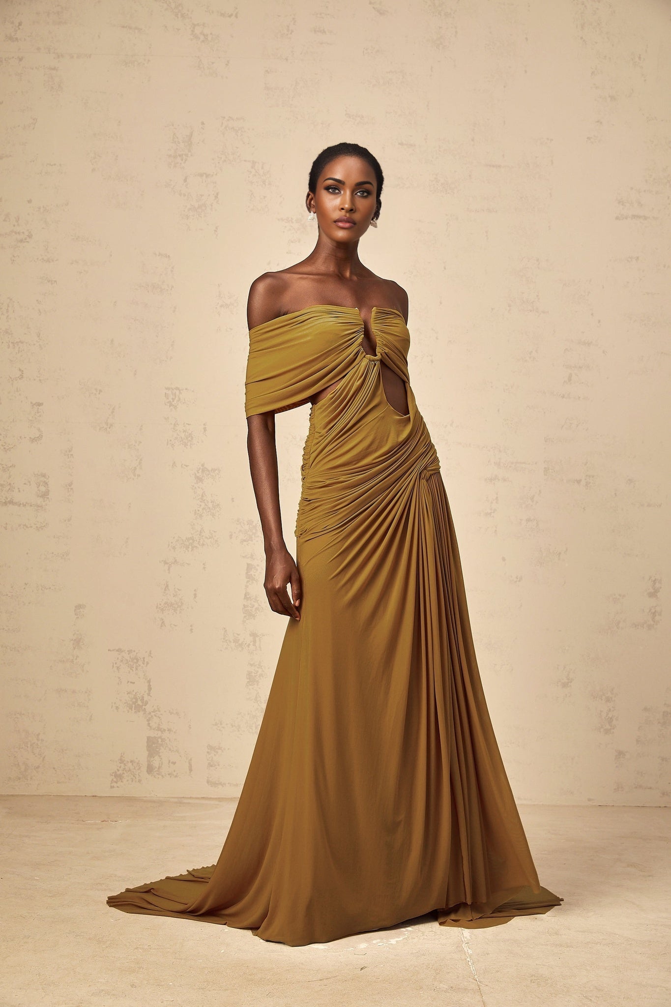 A woman wearing a long ocher maxi dress with offshoulder design ruched details and cutout sections