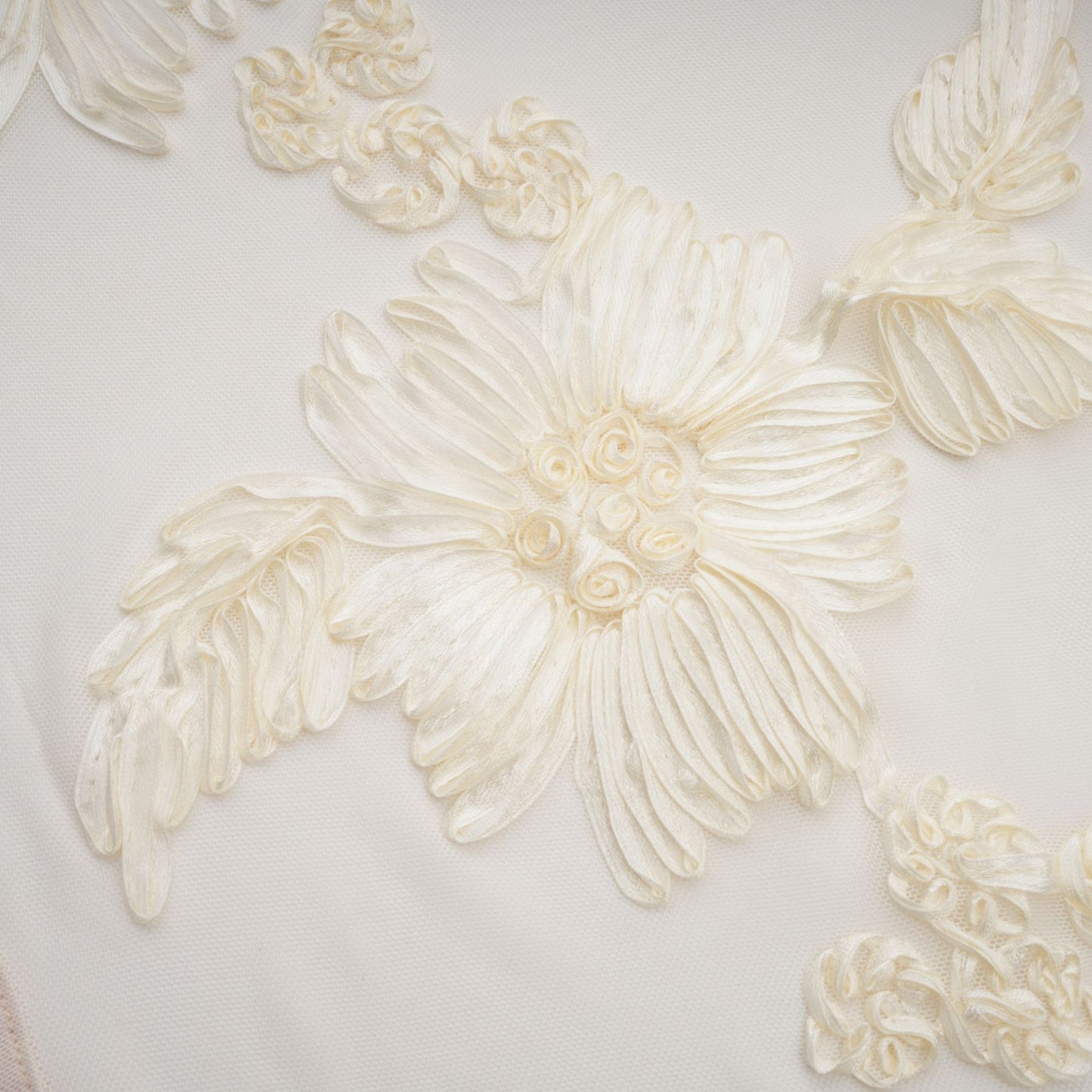 A woman wearing a long offshoulder maxi dress in neutral tones with embroidered details standing against a plain background