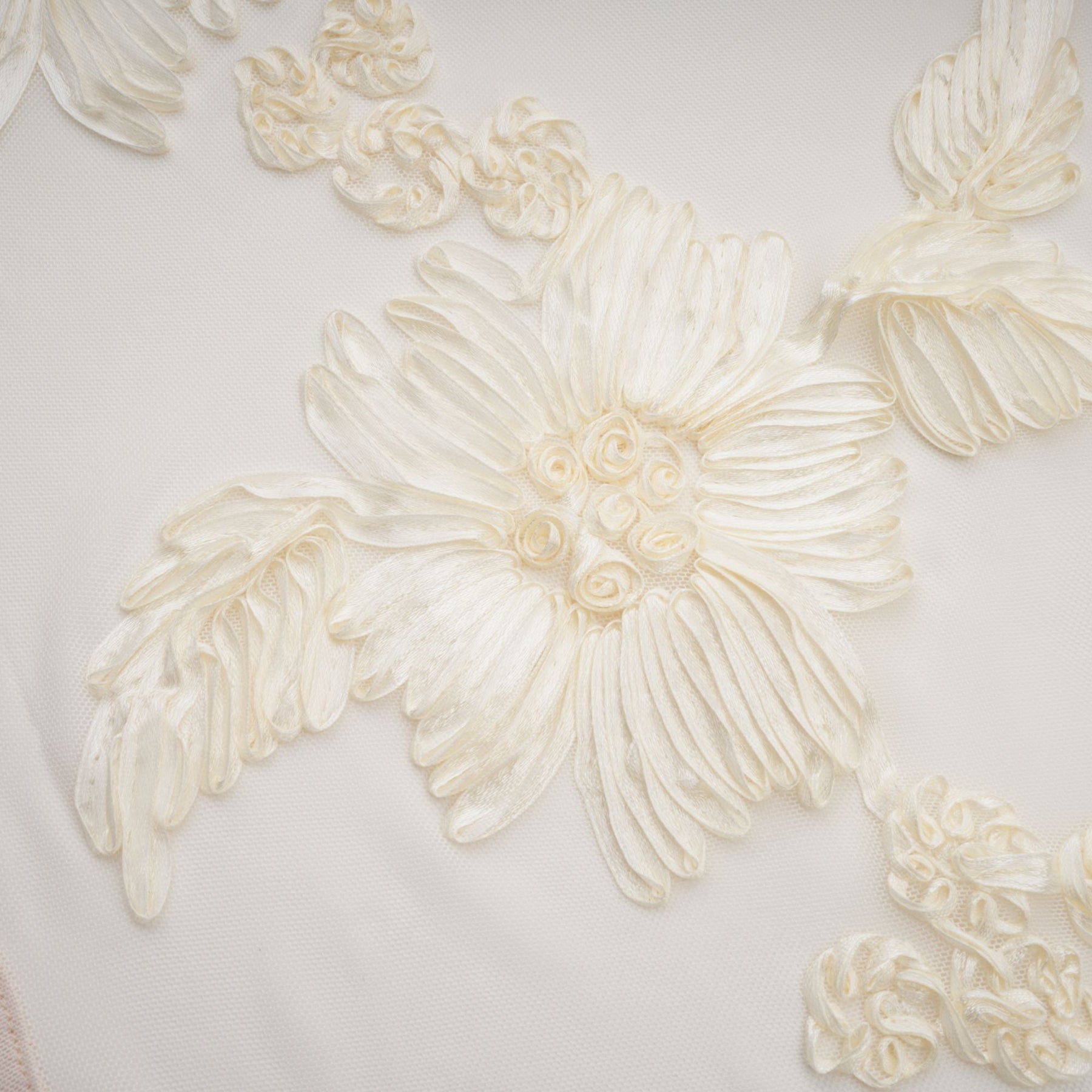 A woman wearing a long offshoulder maxi dress in neutral tones with embroidered details standing against a plain background