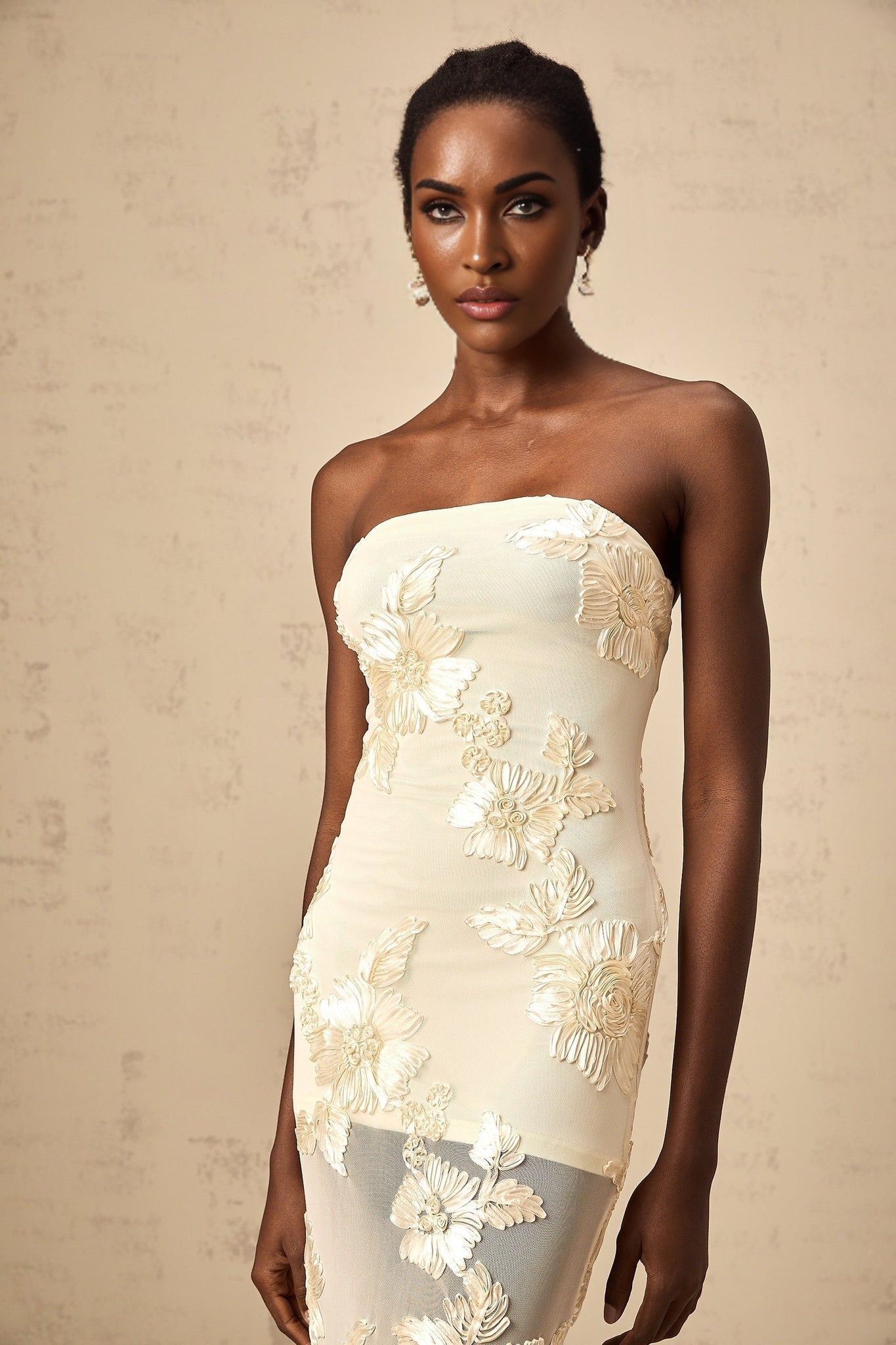 A woman wearing a long offshoulder maxi dress in neutral tones with embroidered details standing in a relaxed pose