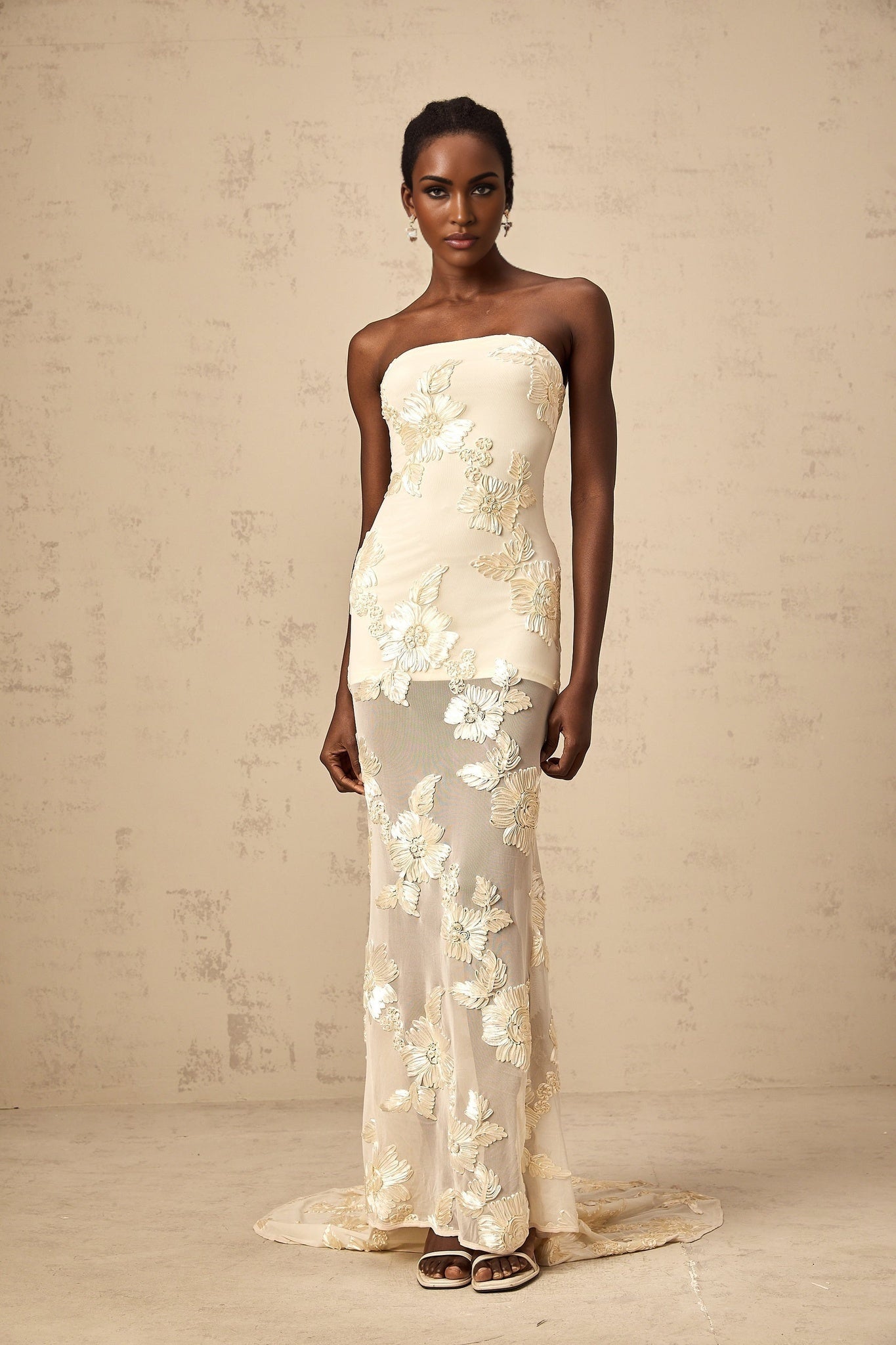 A woman wearing a long offshoulder maxi dress in neutral tones with embroidery detail standing in a relaxed pose