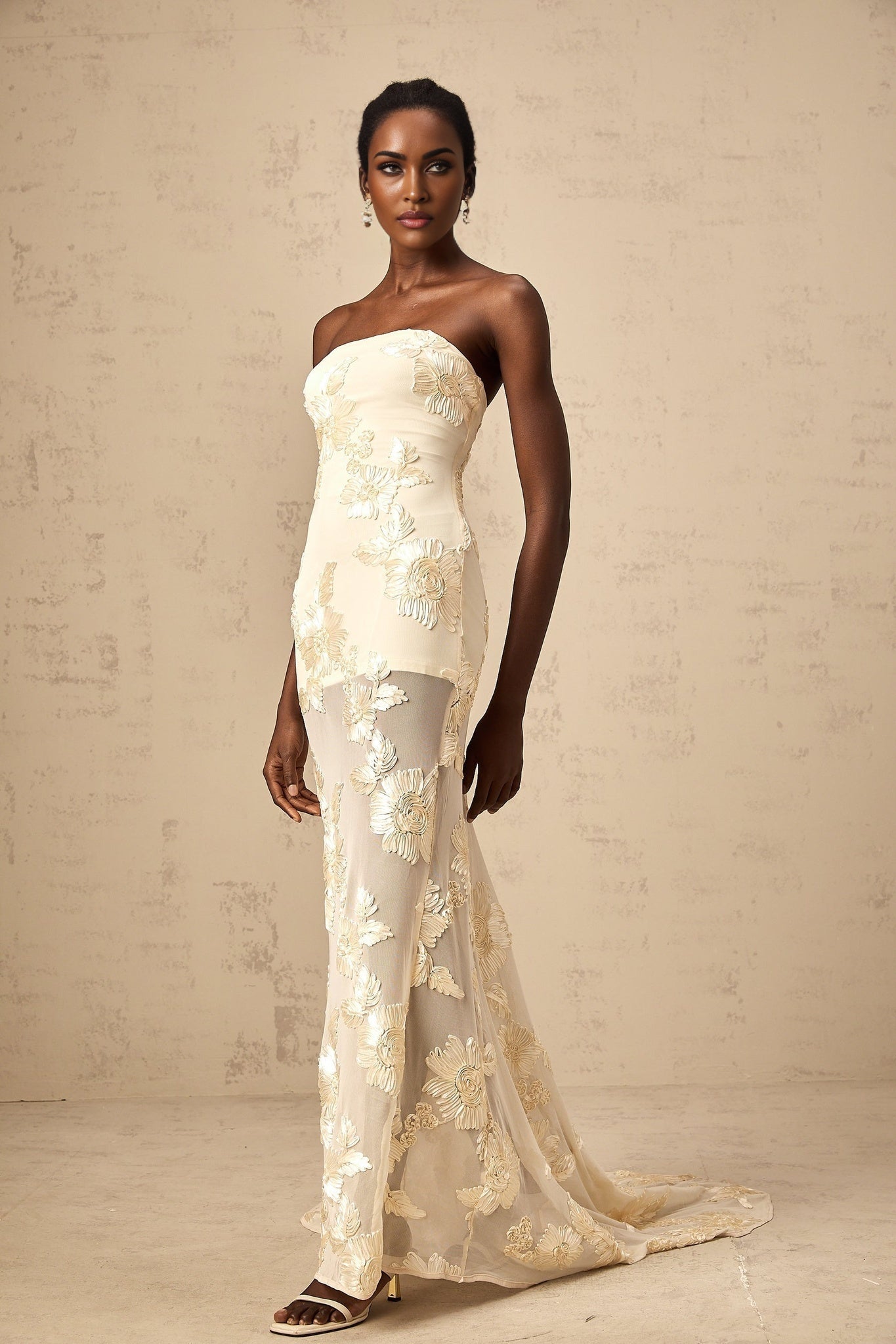 A woman wearing a long offshoulder maxi dress in neutral tones with embroidery details