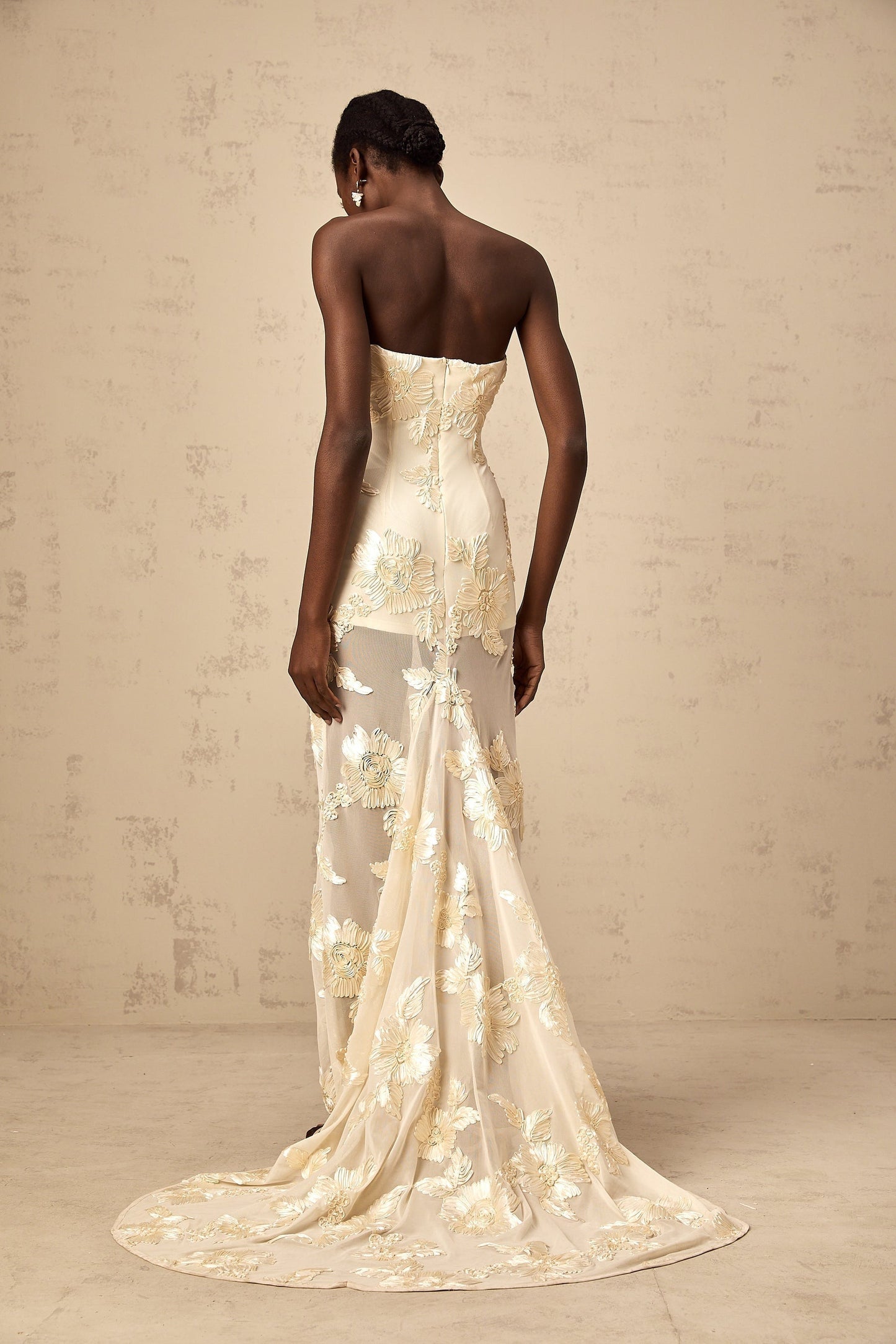 A woman wearing a long offshoulder maxi dress in neutral tones with embroidery details