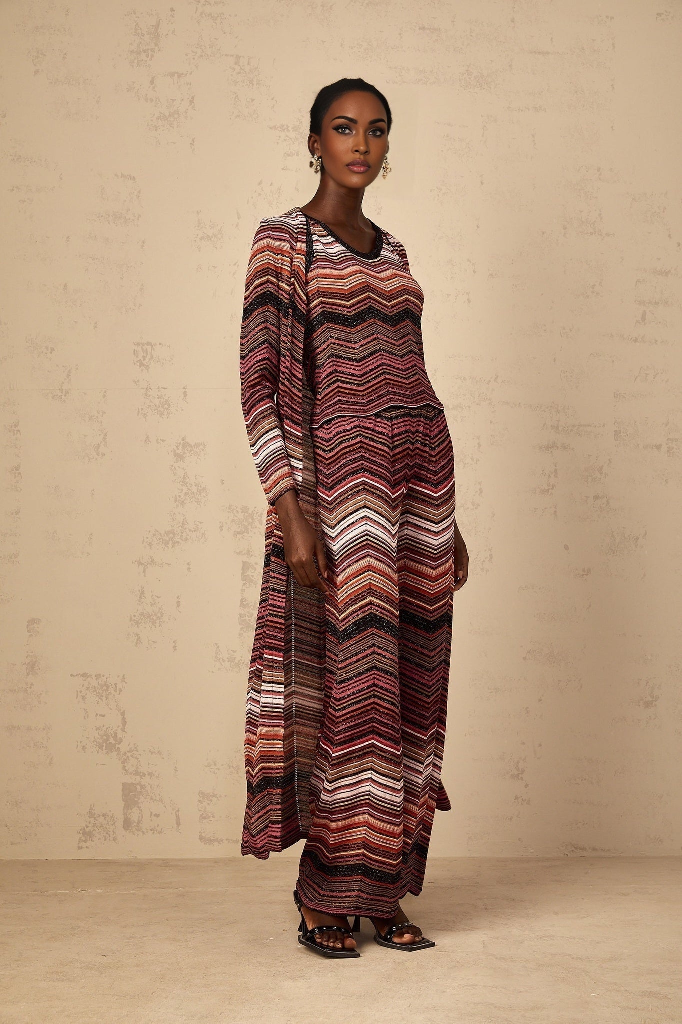 A woman wearing a long red cardigan with white stripes knitted pattern open front design and ribbed cuffs