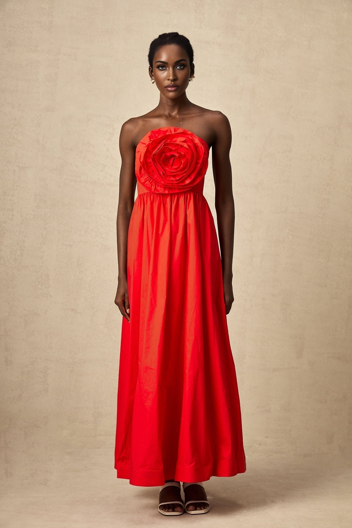 A woman wearing a long red dress with 3d floral petal ruffles cascading down the length of the maxi gown