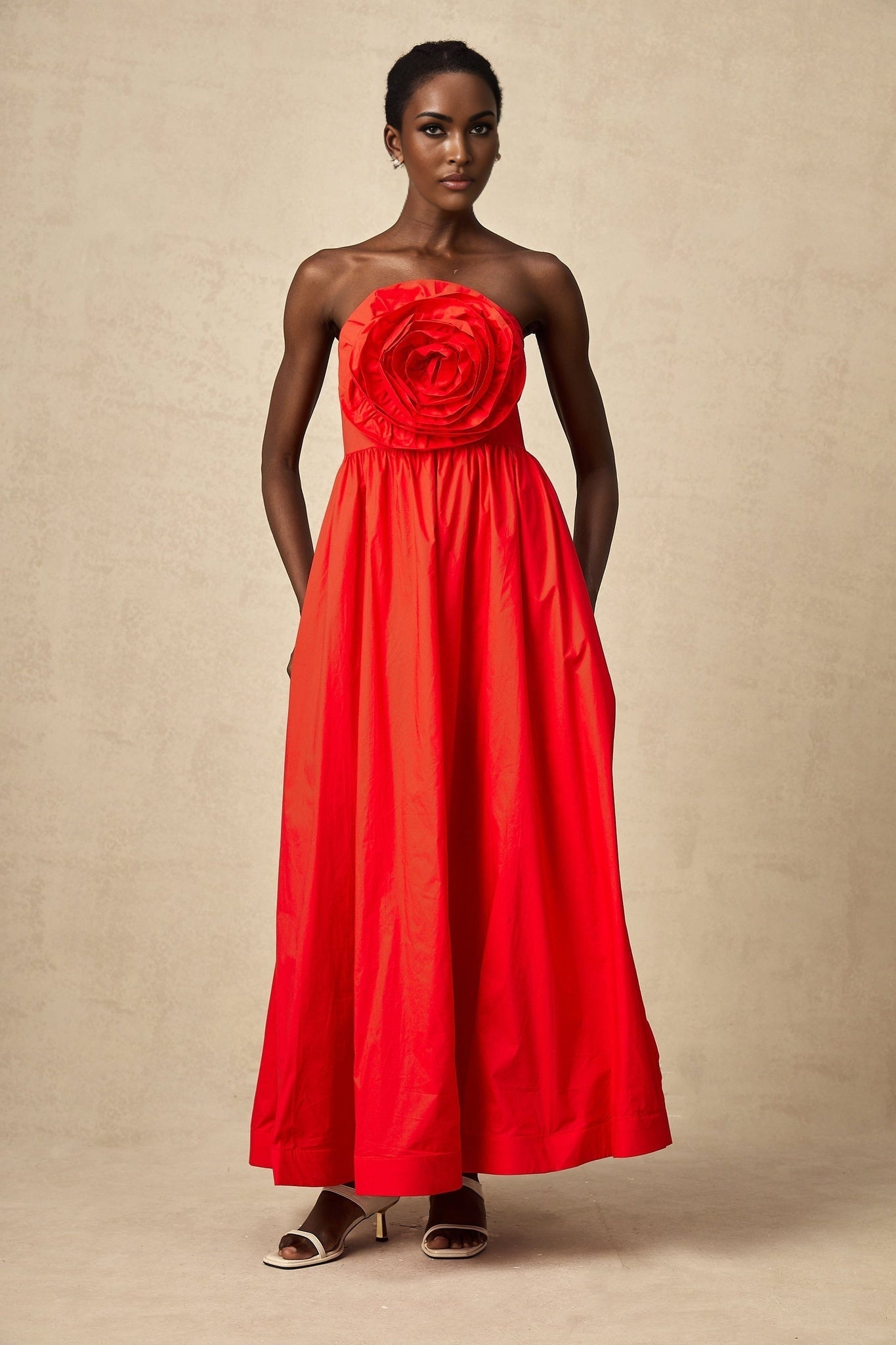 A woman wearing a long red dress with layered 3d petal ruffles cascading down the length of the flowy maxi skirt
