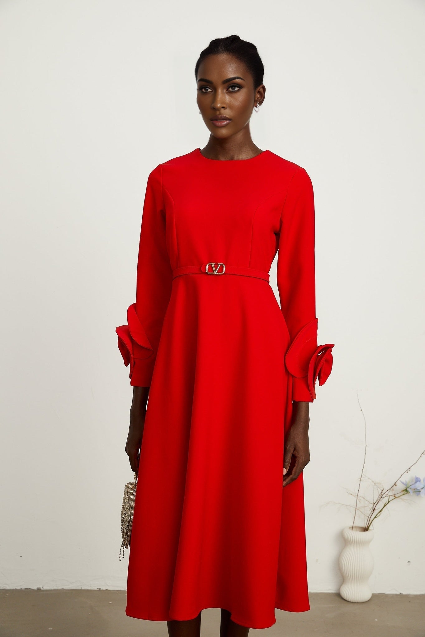 A woman wearing a long red dress with long sleeves and floral embellishments standing in a neutral setting