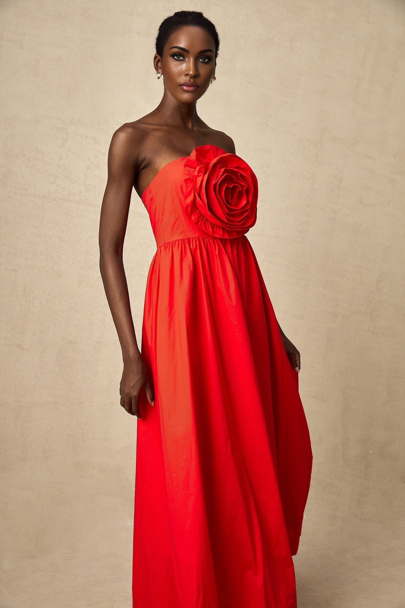 A woman wearing a long red maxi dress with cascading 3d floral petal ruffles covering the bodice and skirt