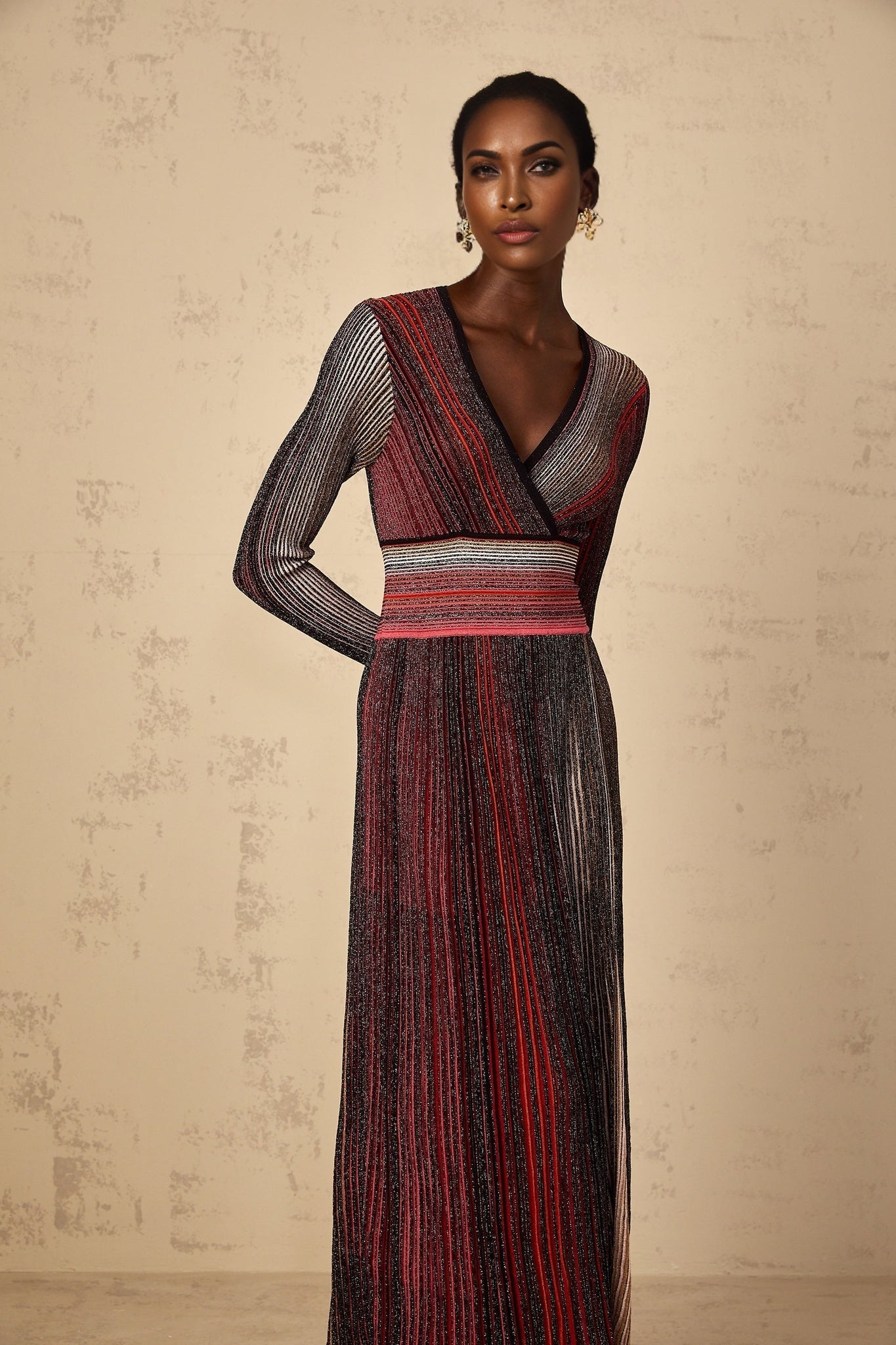 A woman wearing a long red maxi dress with long sleeves and vertical sequin stripes standing against a plain background