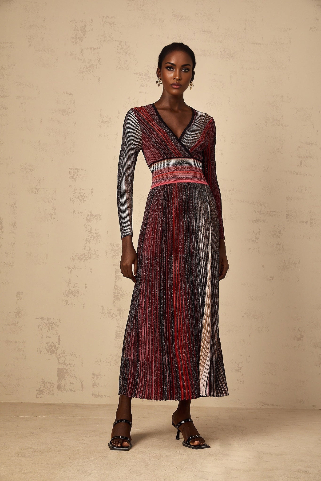 A woman wearing a long red maxi dress with long sleeves and vertical sequin stripes that shimmer in the light The dress has a knit texture and flows to the floor