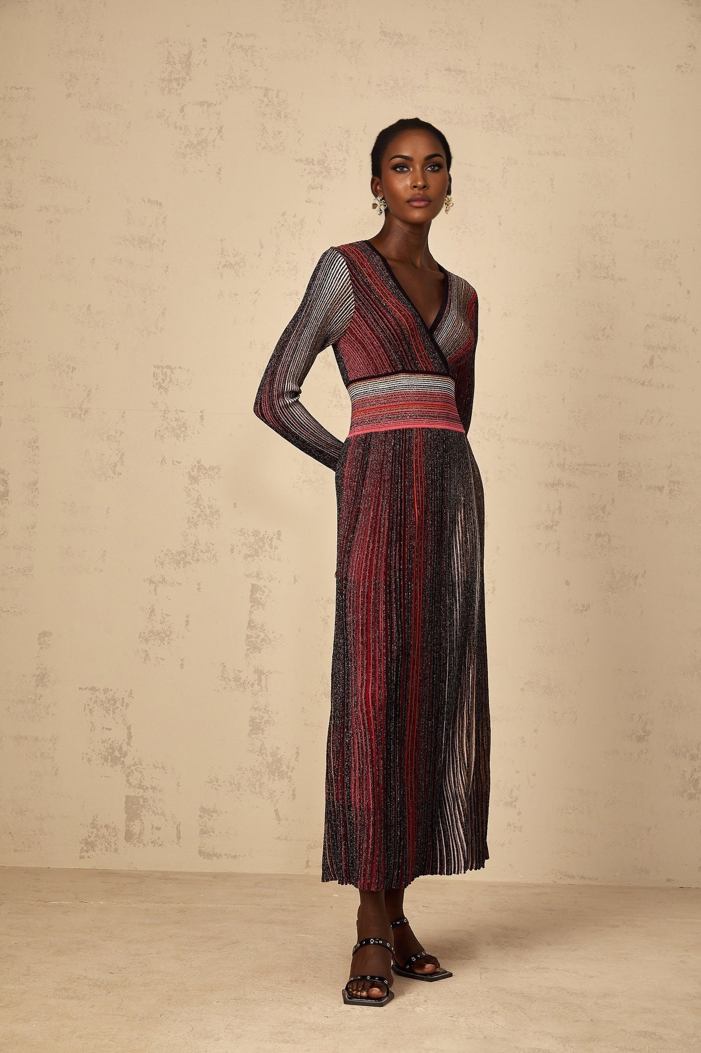A woman wearing a long red maxi dress with long sleeves featuring sequin striped details and a knit fabric